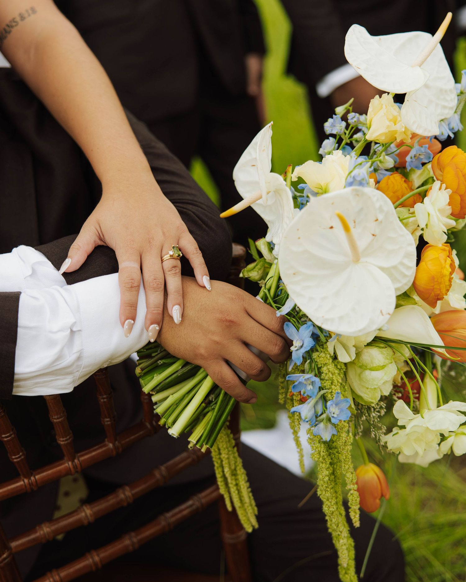 Wedding bouquet with white anthurium flowers and hands showing rings.