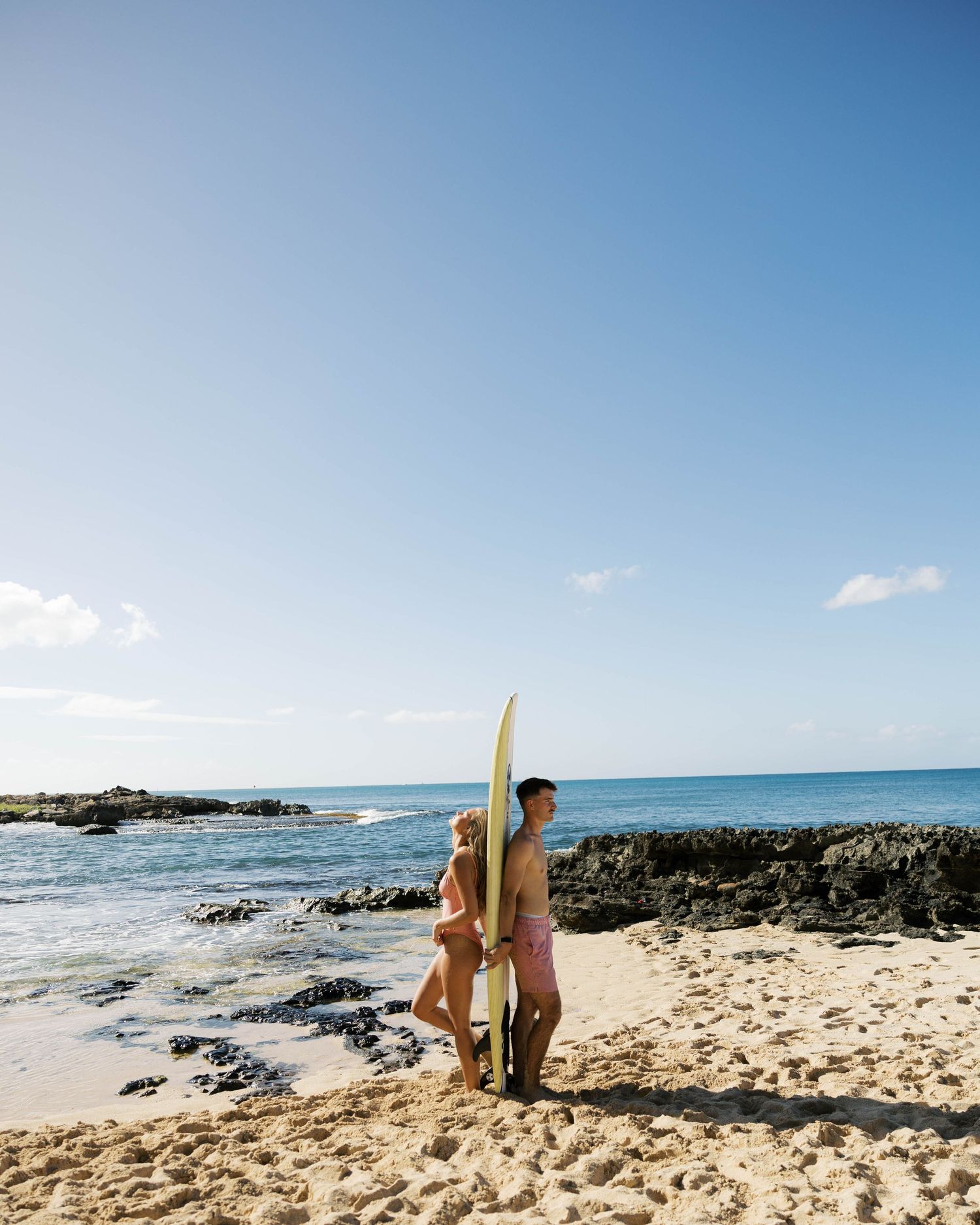 Panoramic view of a Hawaiian beach with surfers, volcanic rocks, and crystal clear waters.