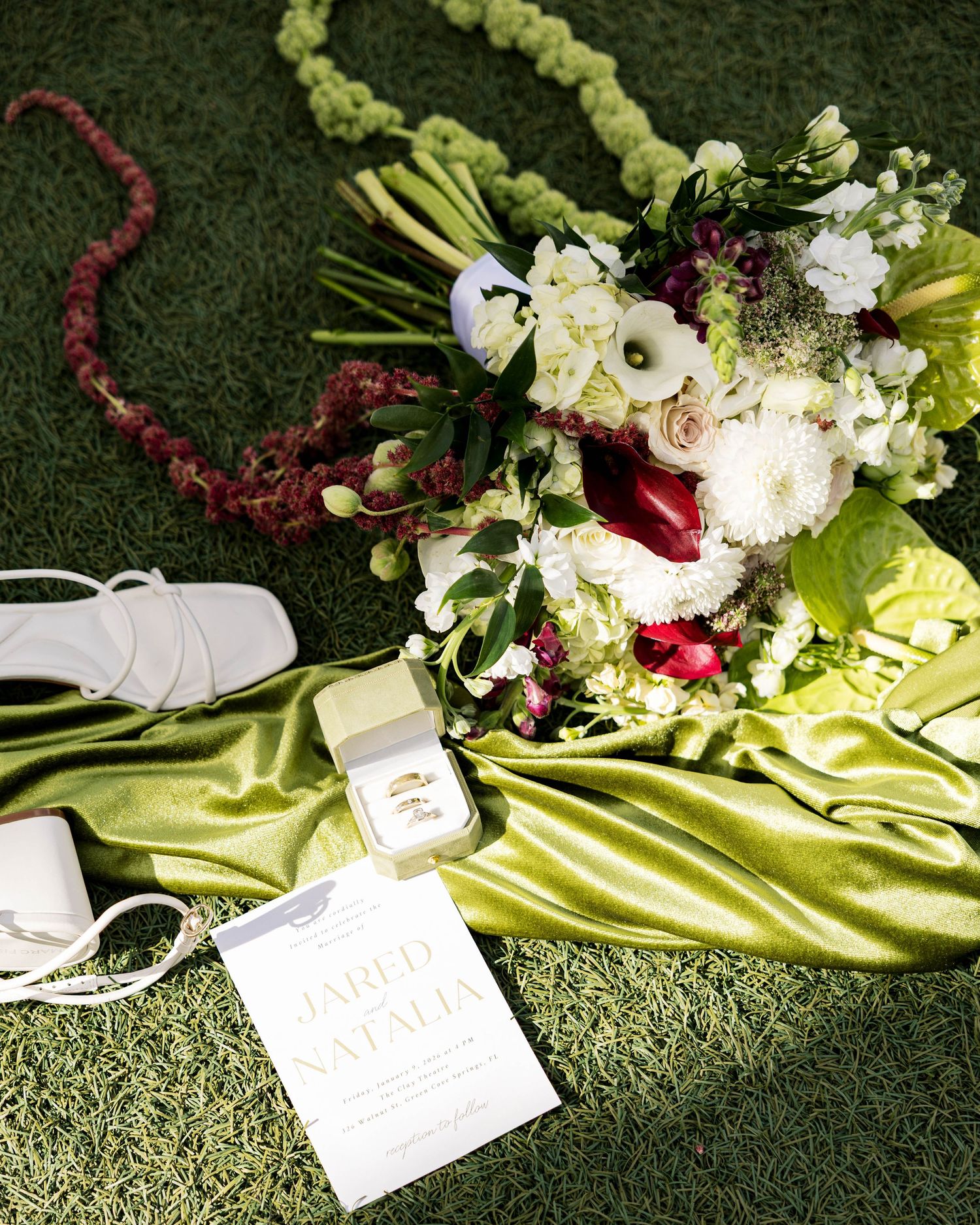 Wedding floral arrangement with white blooms and burgundy accents on lime green silk fabric.