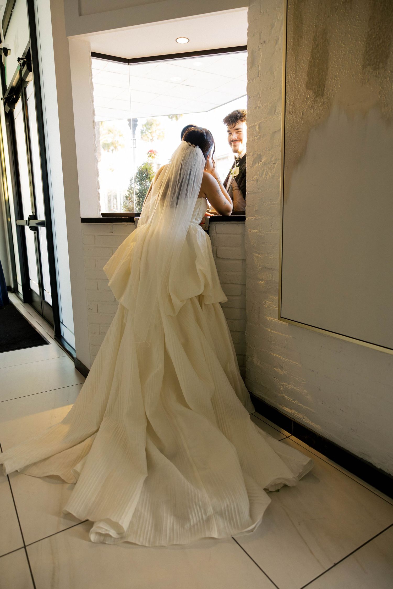 Flowing white wedding dress train trailing on tiled floor.