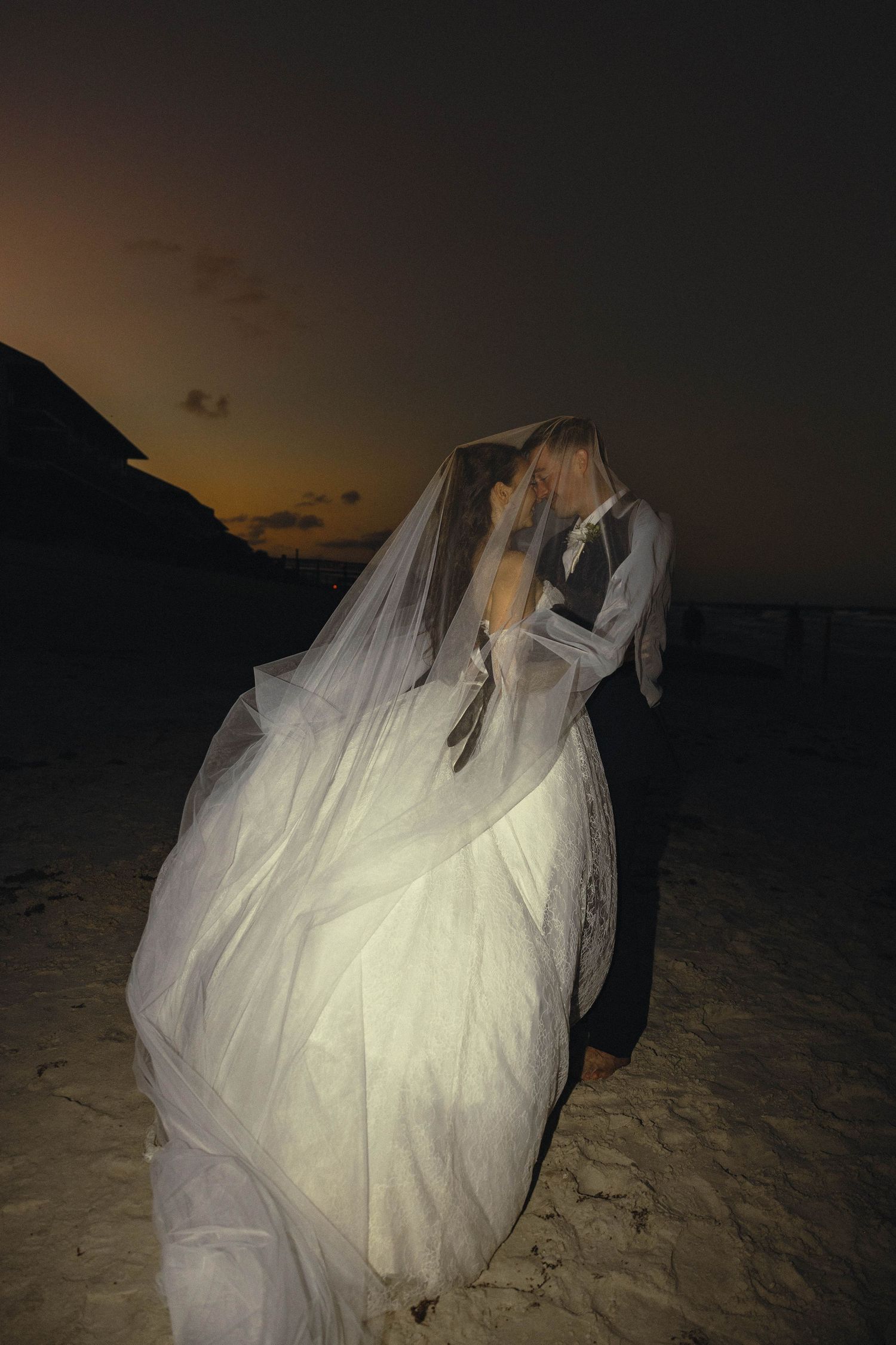 Dramatic nighttime beach photos showing a flowing white wedding dress illuminated against the dark sand.
