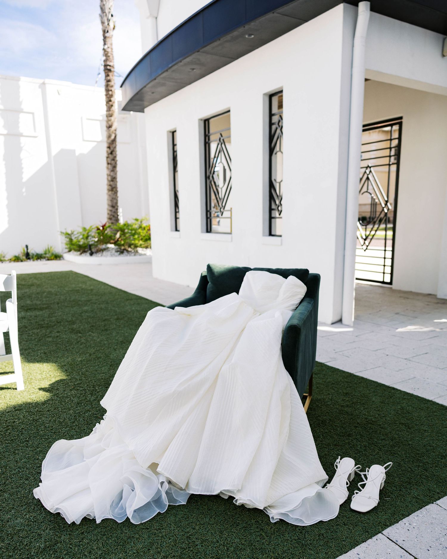 White wedding dress train flowing across outdoor courtyard with white columns and artificial grass.