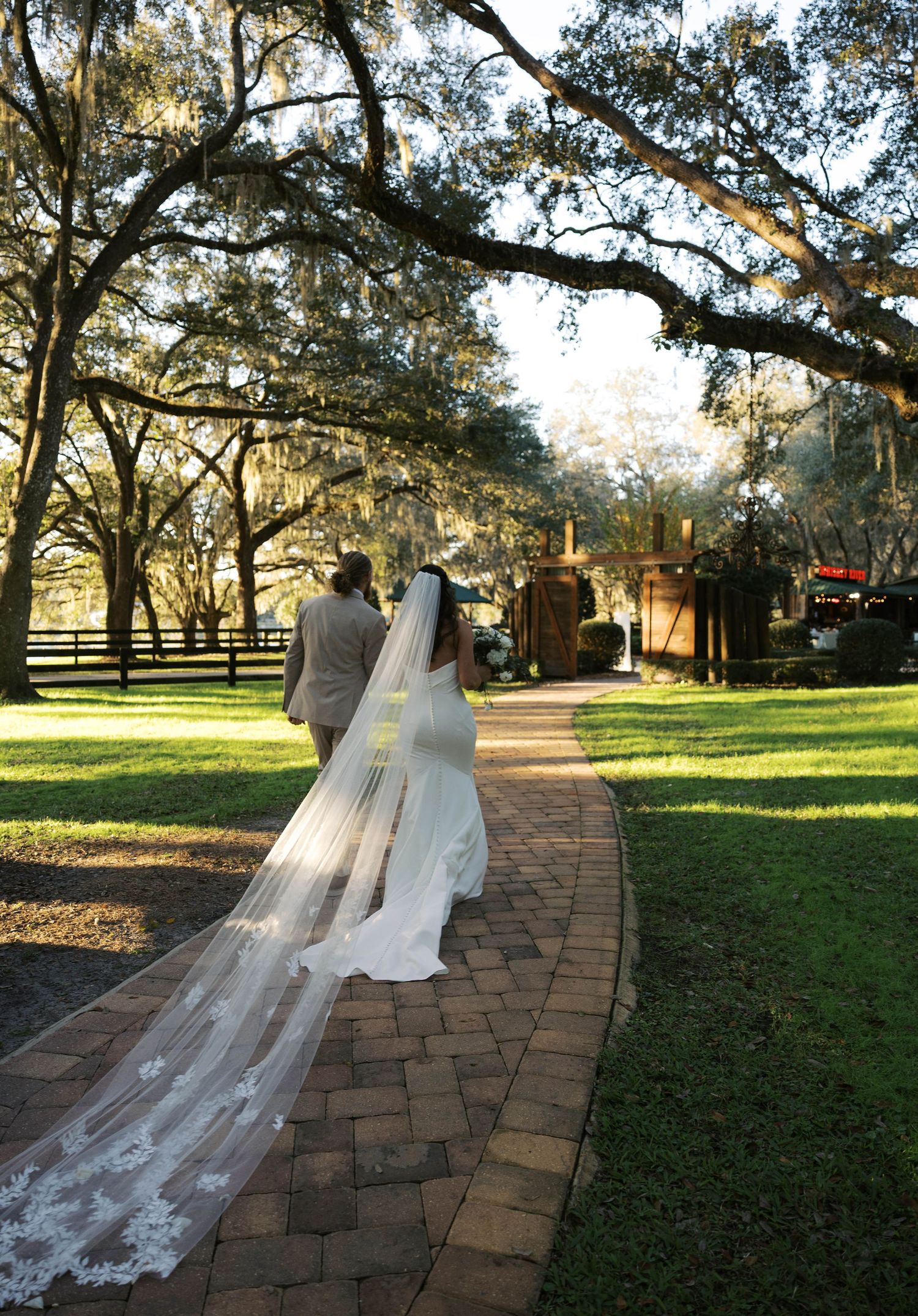 Couple walks down brick pathway under Spanish moss draped trees.