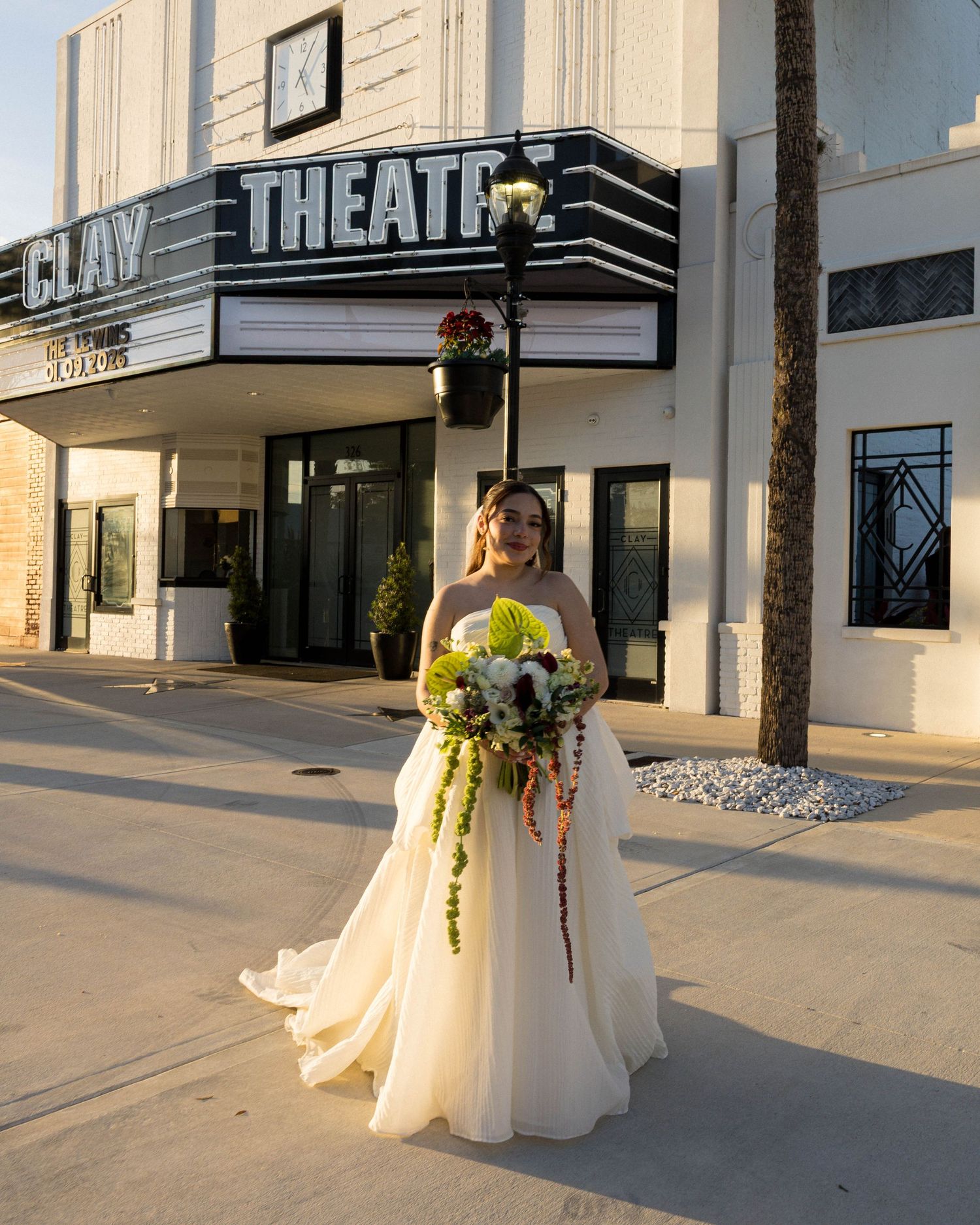 A radiant bride poses with her bouquet outside the historic Clay Theatre entrance.