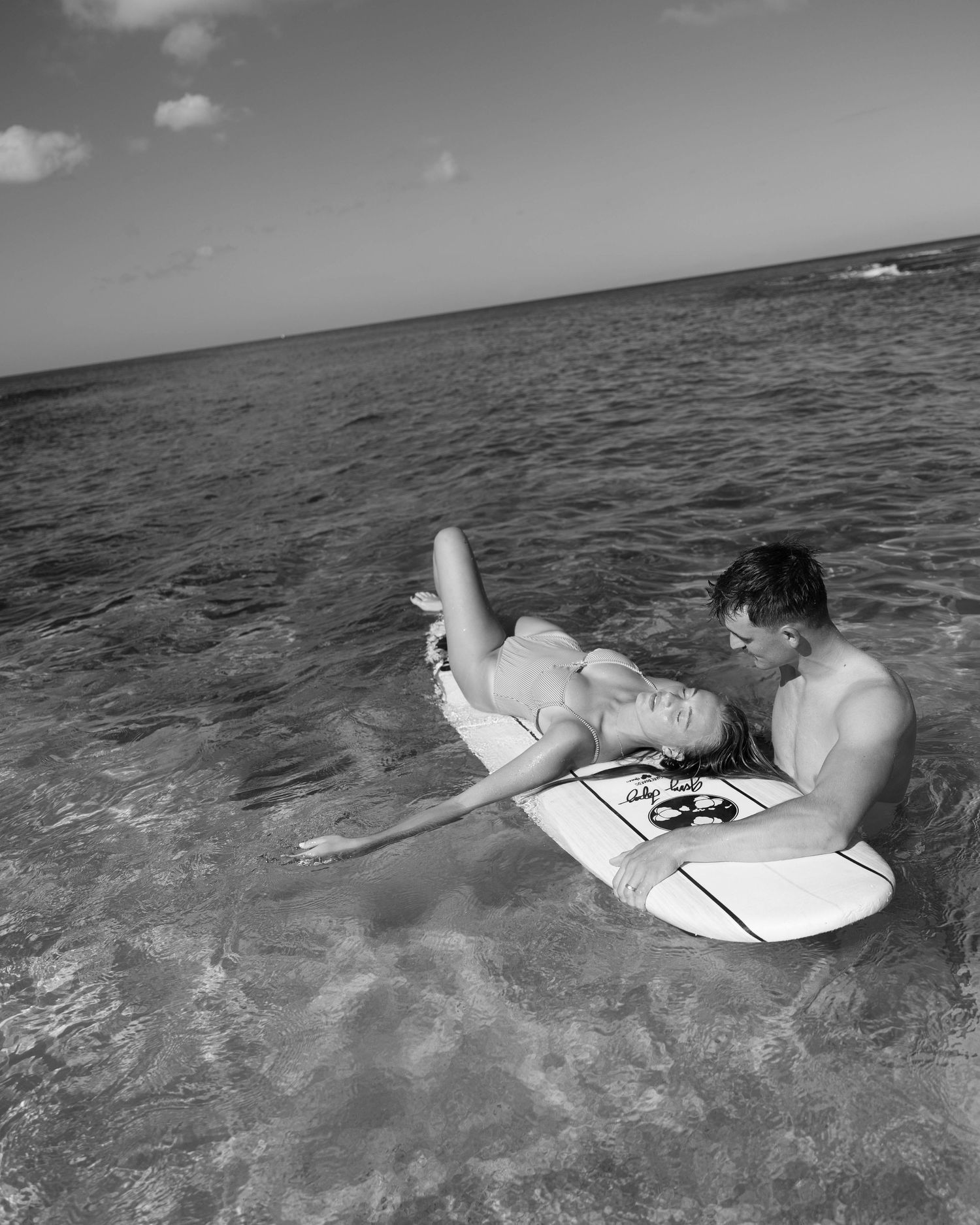 Black and white scene of surfers lying on boards in rolling ocean waves.