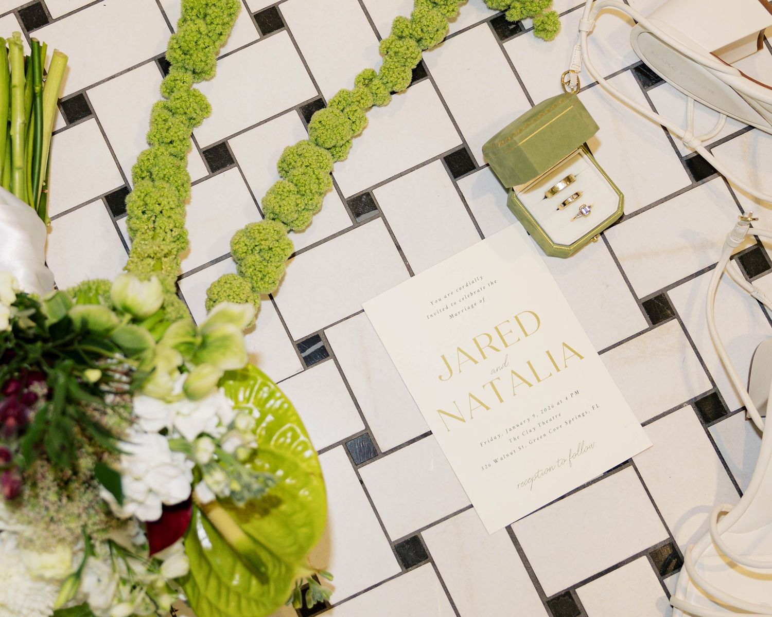 Artistic wedding details with floral arrangements and place cards on white geometric tile pattern.