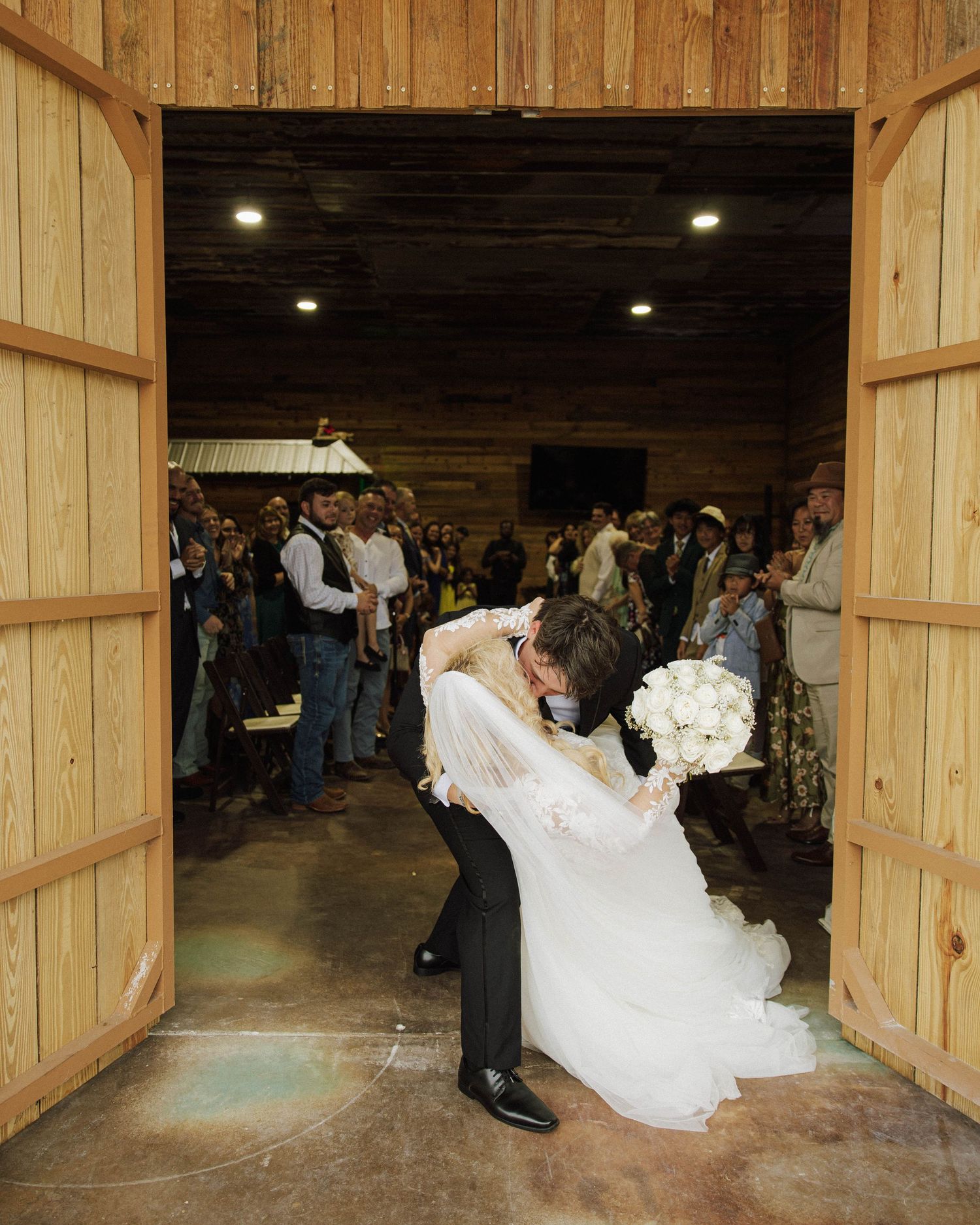Wedding couple dances in a rustic wooden barn venue surrounded by guests.