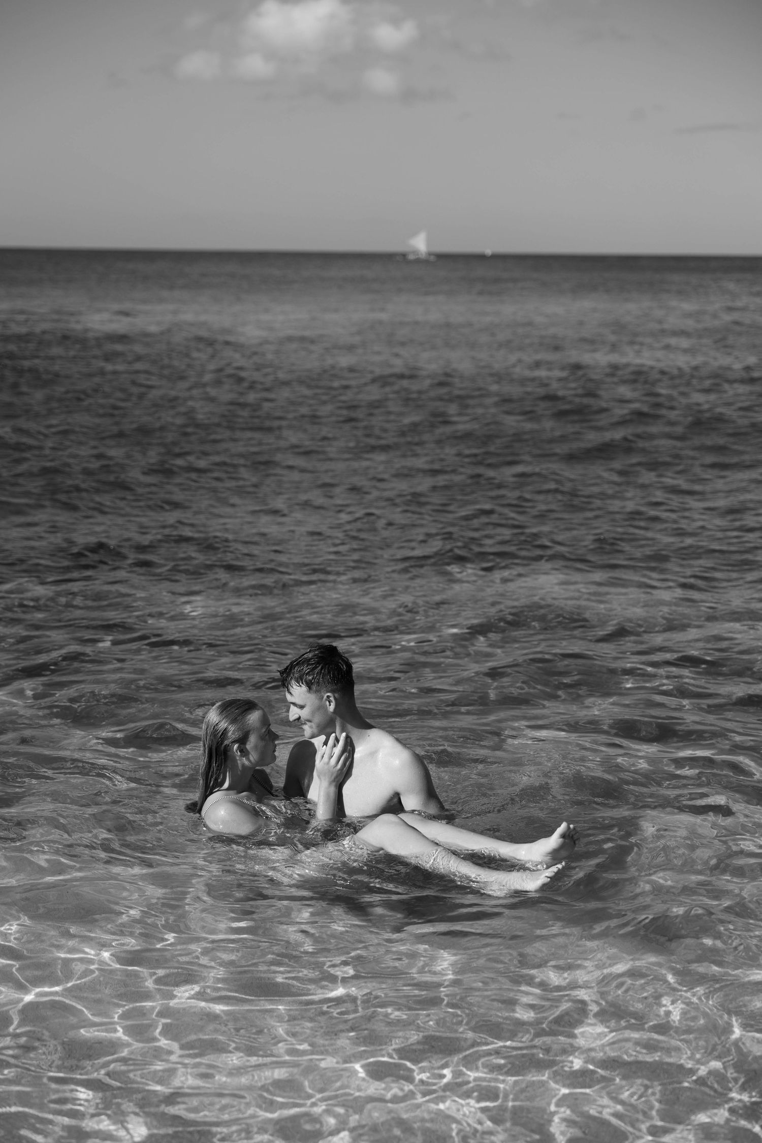 Black and white image of people swimming in tropical waters with horizon in view.