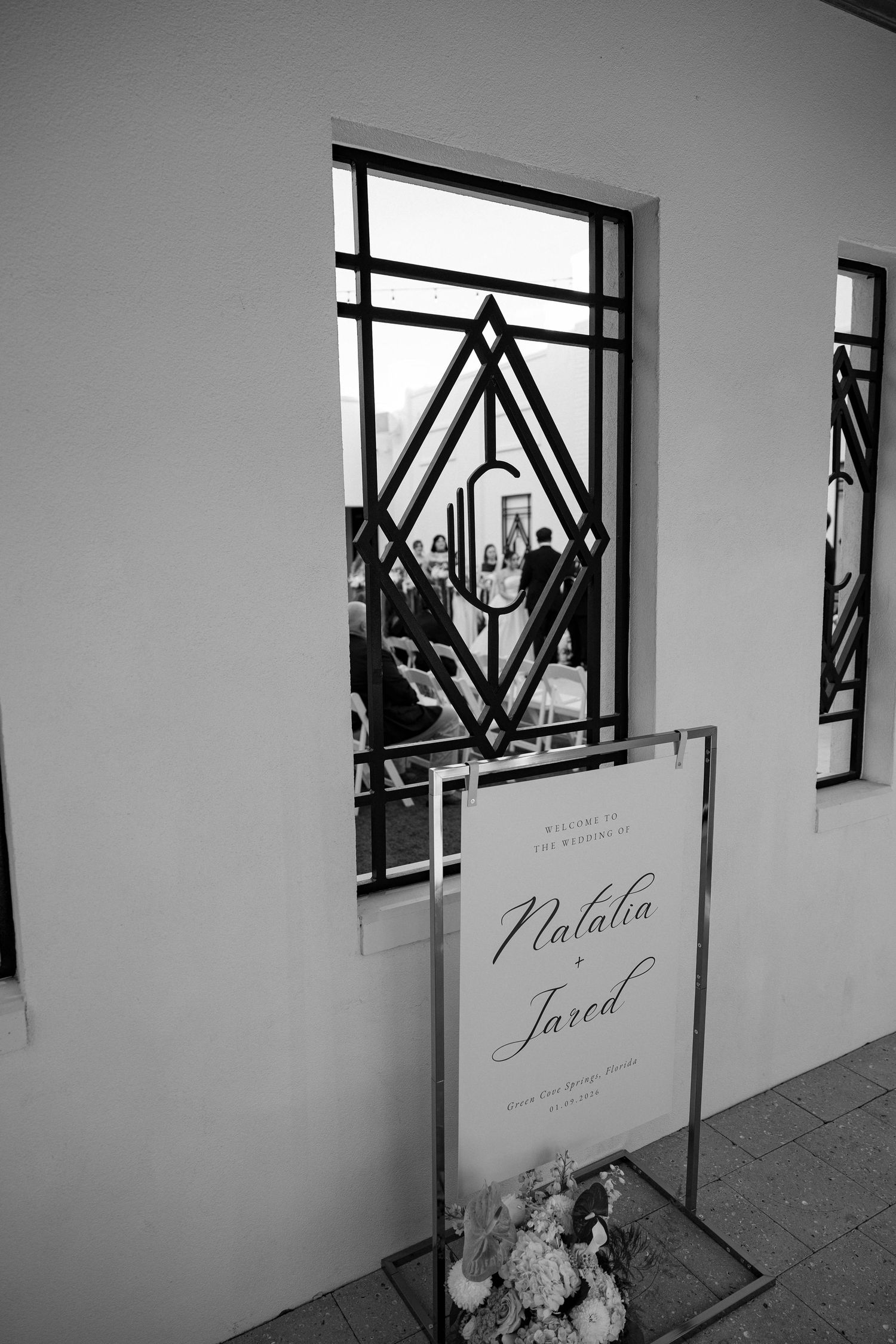 Black and white photo of geometric window design with wedding welcome sign below.