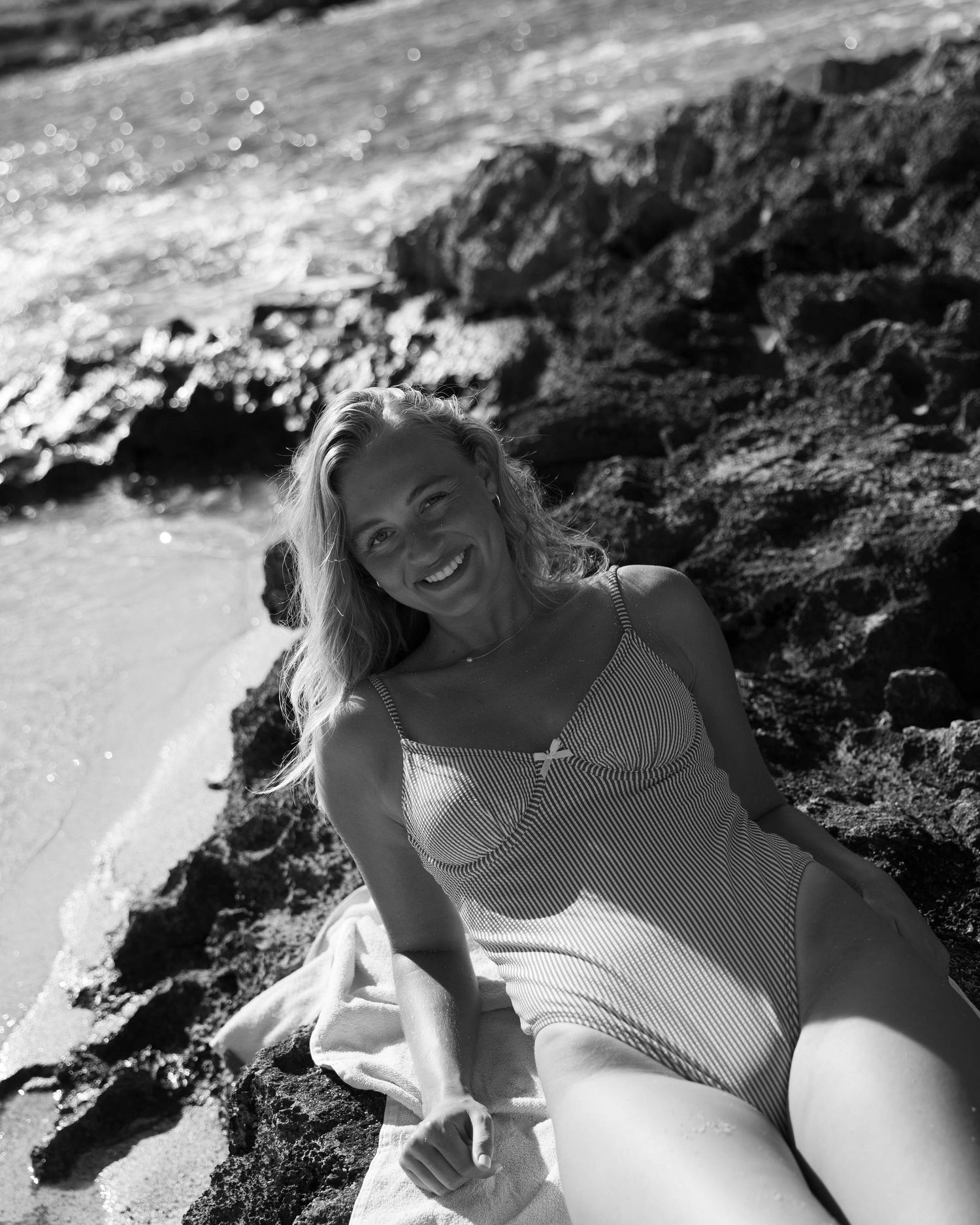 Black and white photos of someone lounging on rocky beach in swimwear.