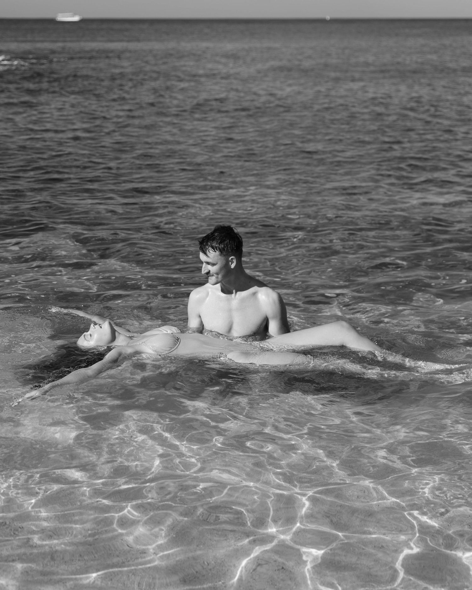 Black and white photo of people floating in crystal clear ocean waters.