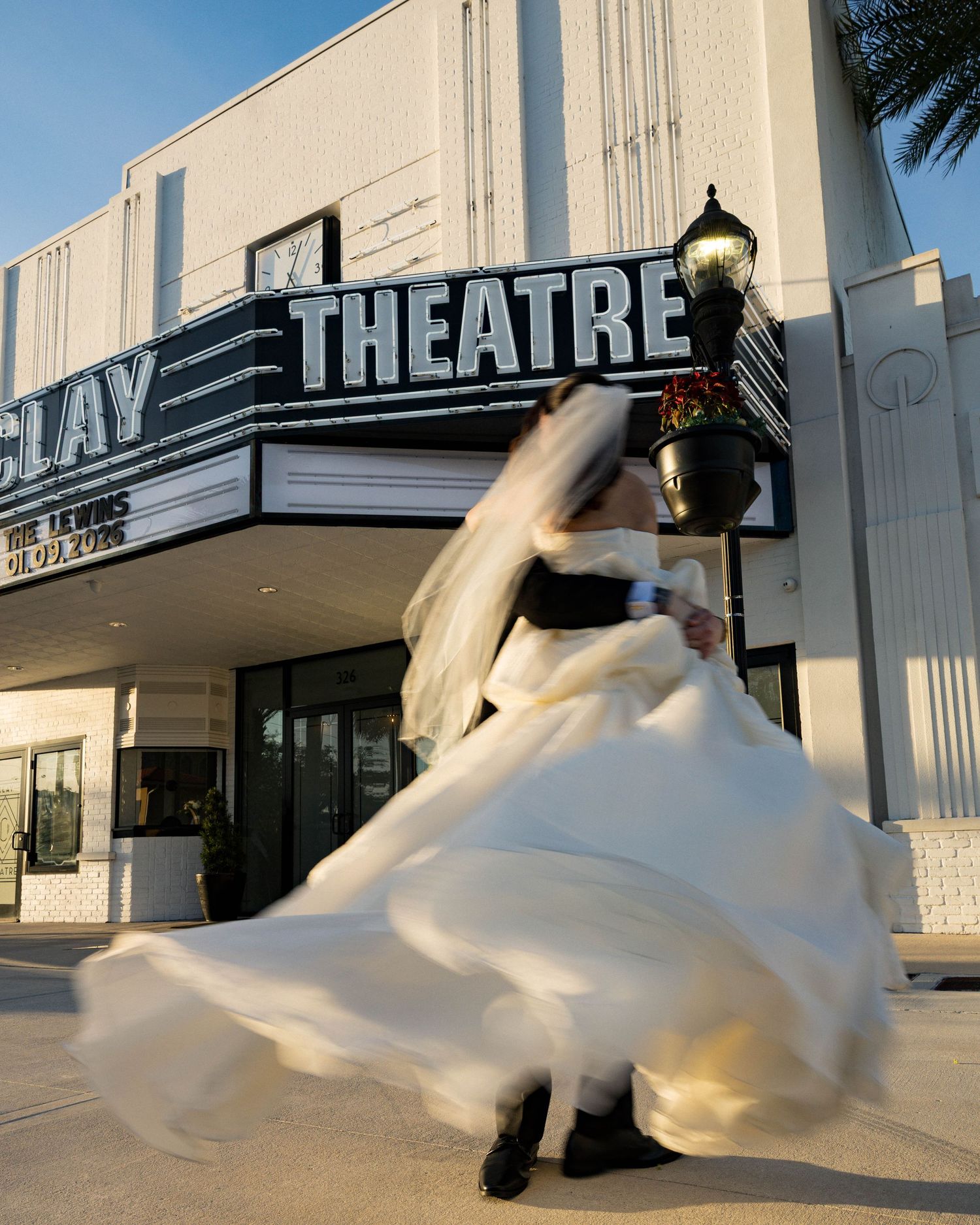A bride's dress twirls dramatically beneath the Clay Theatre sign in an artistic wedding photo.