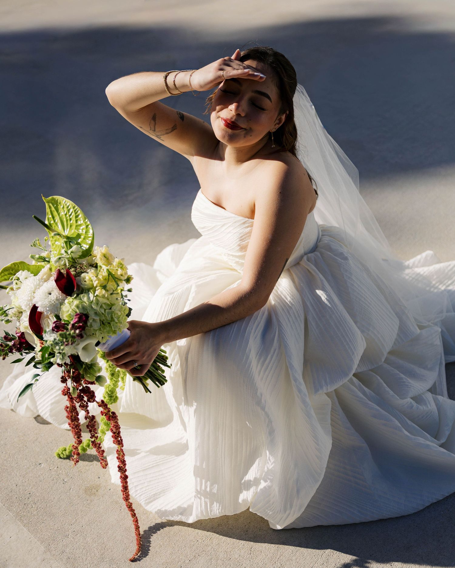 Modern bridal portrait with sunlit shadows showing details of dress and bouquet arrangement.