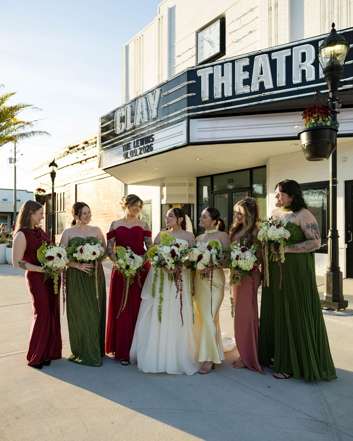 Wedding party poses for formal photos outside vintage theater with palm trees in background.