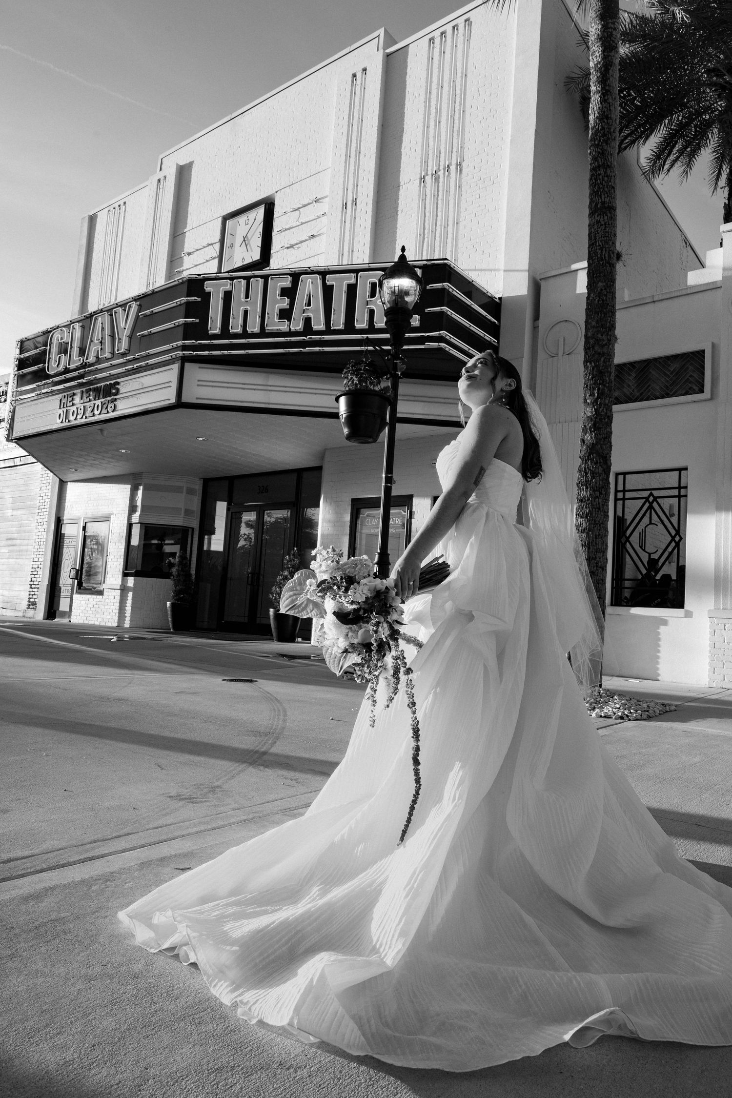 Black and white image of a bride in a flowing dress spinning outside a classic theater.