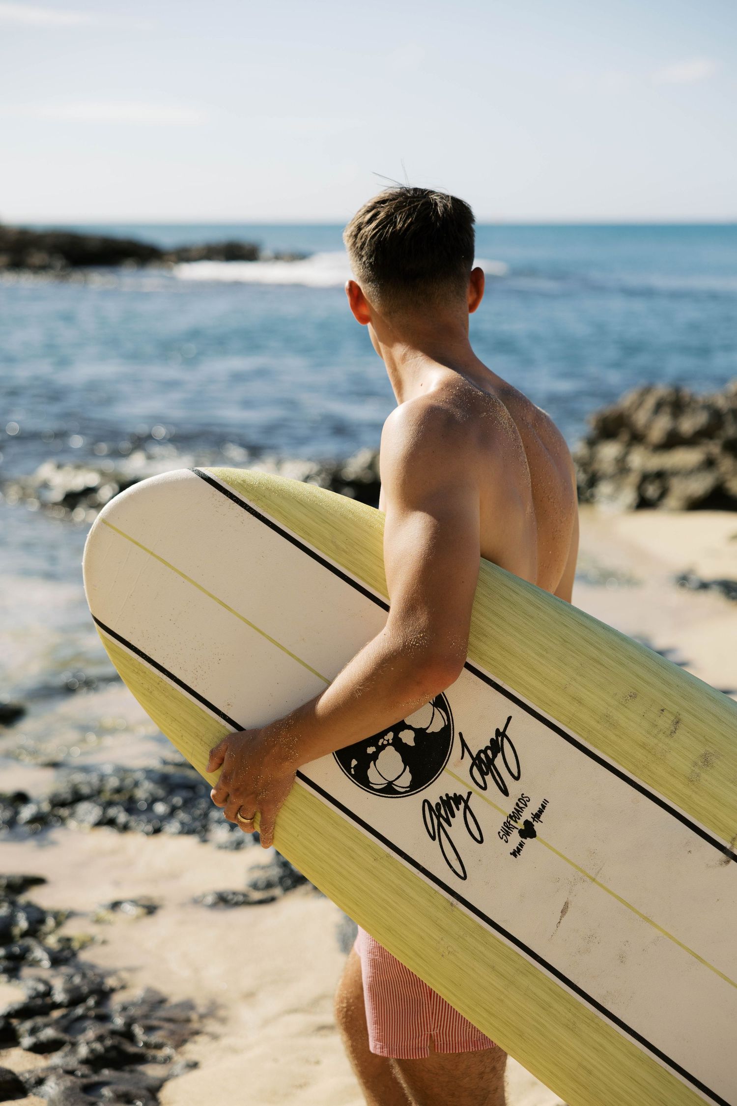Close-up of surfboard with signature being carried along rocky beach.