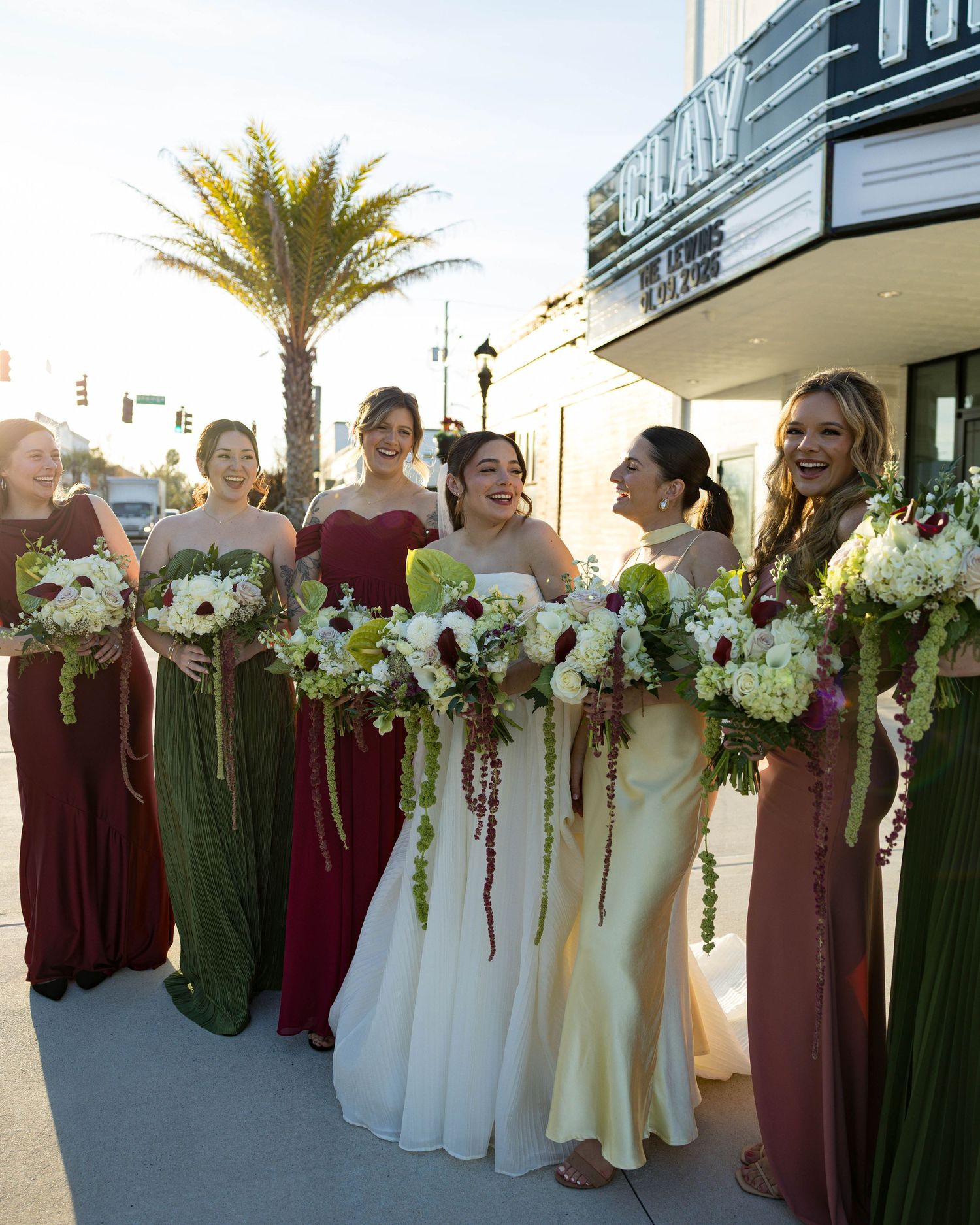 Bridal party members display white floral bouquets while lined up against theater exterior.