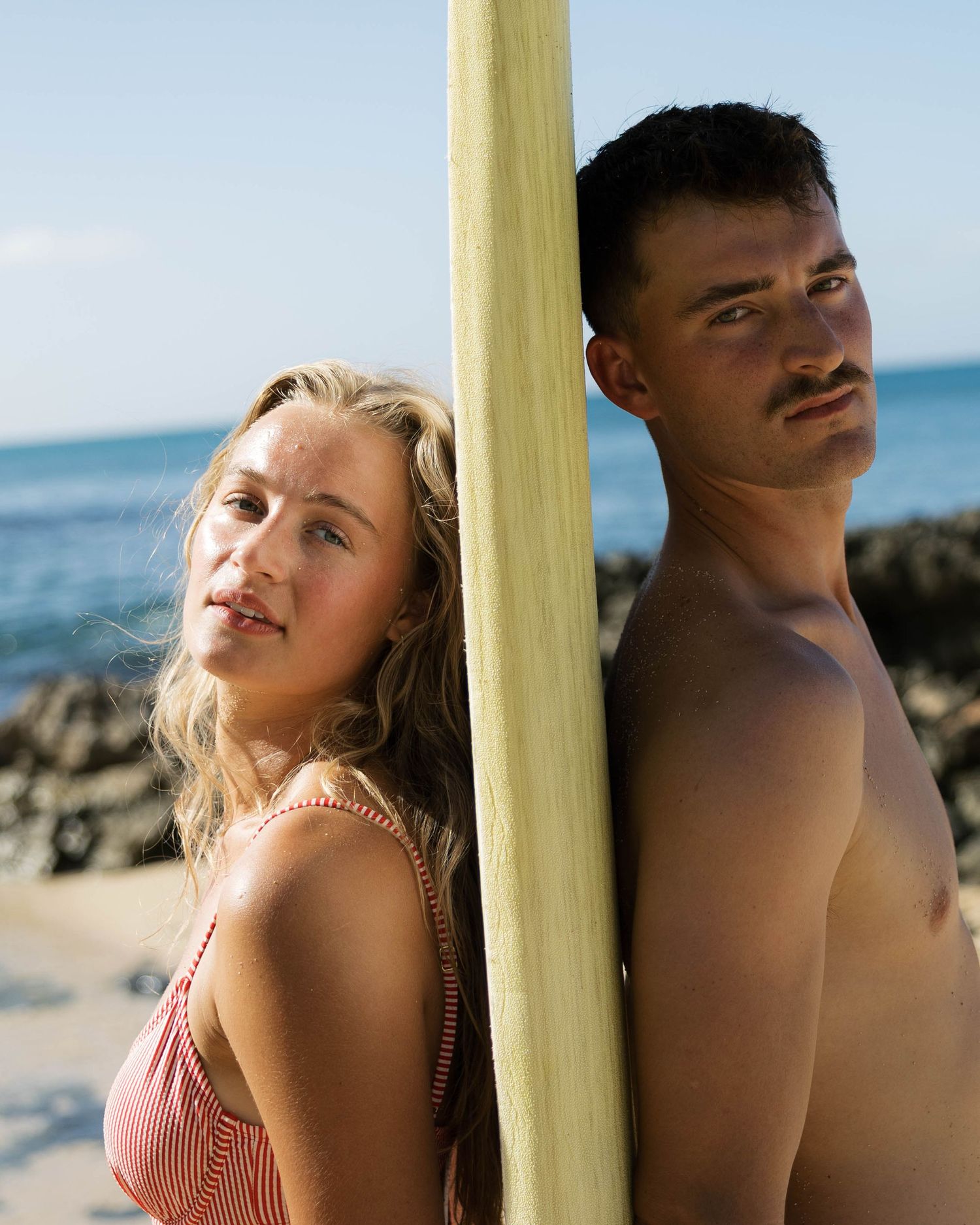 Beachside portrait series with surfboard against blue ocean backdrop.