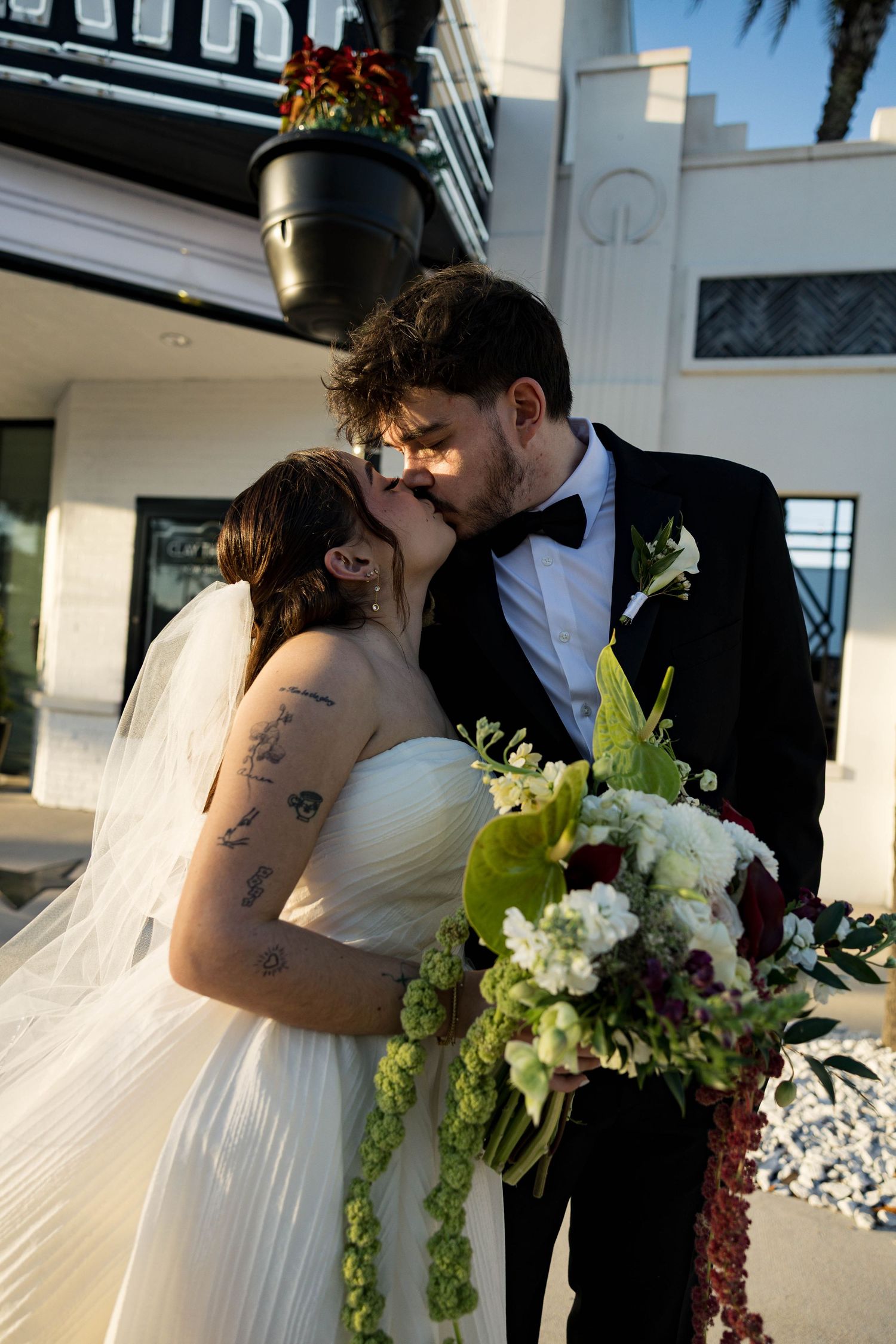 A wedding couple shares a romantic kiss outside the Clay Theatre with a beautiful floral bouquet.