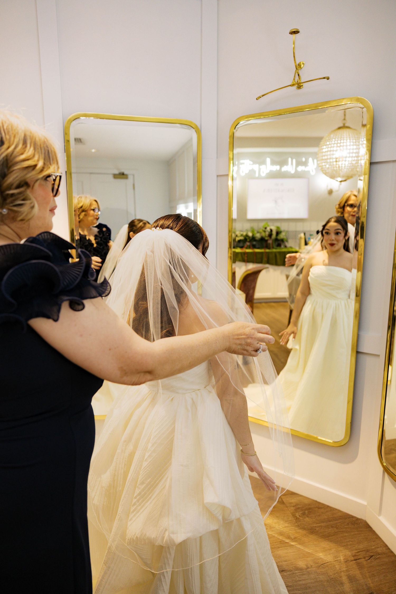 Wedding dress fitting session in an elegant boutique with gold-framed mirrors.