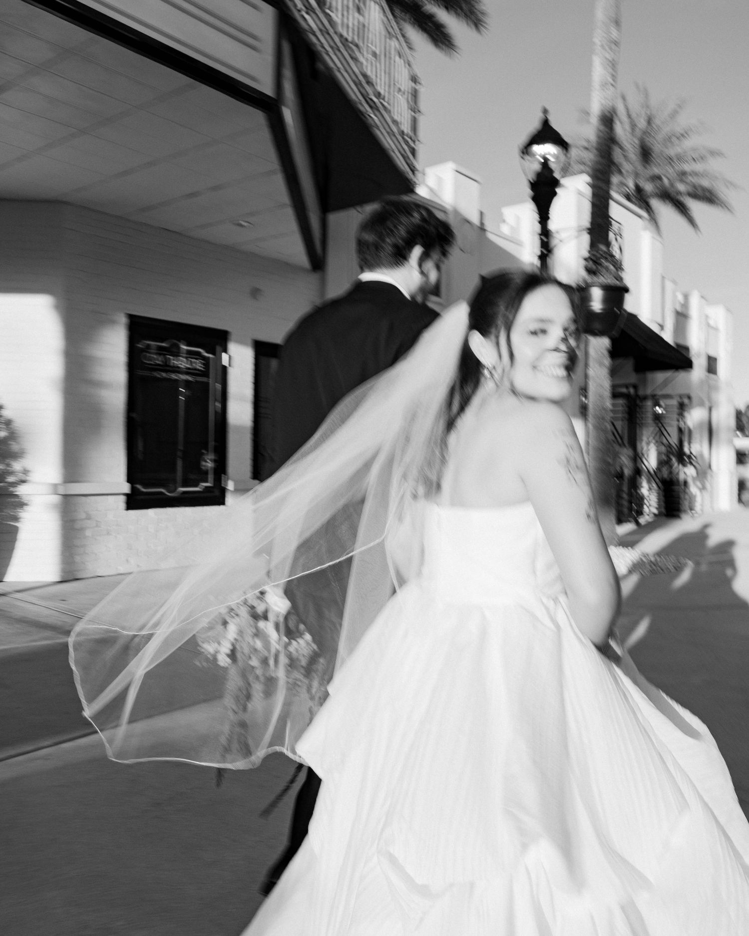 Black and white photo of a bride in a ballgown twirling outside a building.