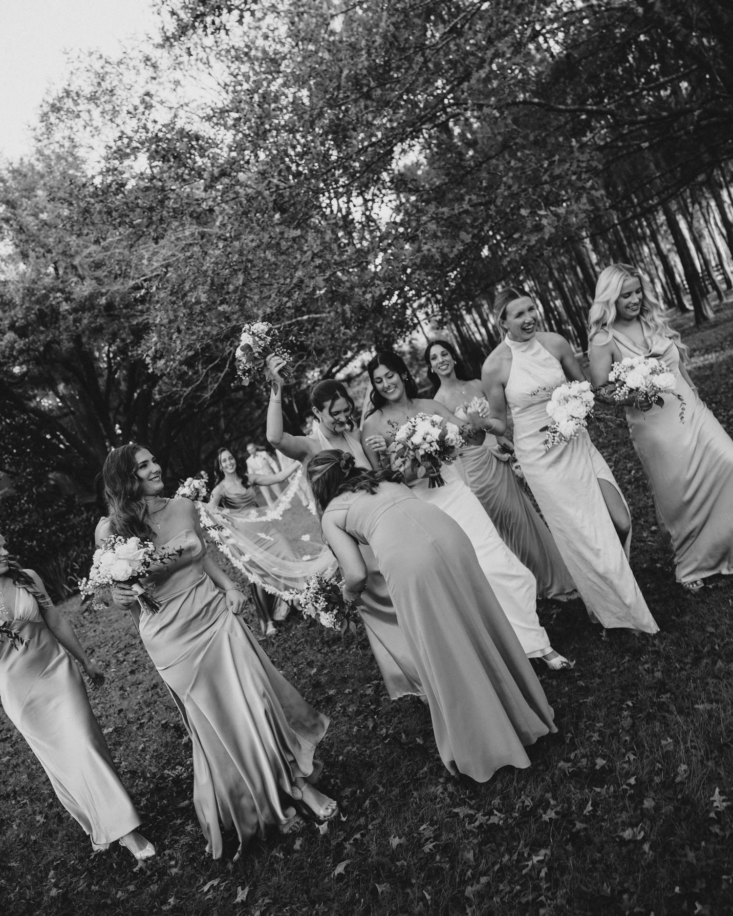 Wedding party in light colored dresses poses playfully outdoors in black and white.