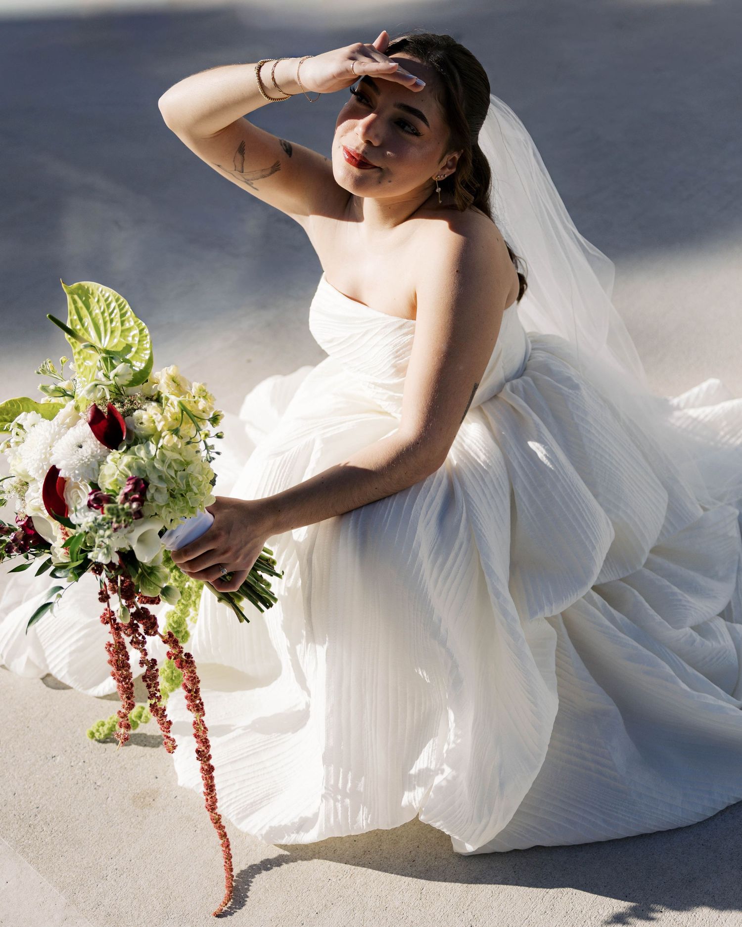 Elegant bridal portrait with white dress and burgundy floral bouquet in natural sunlight.