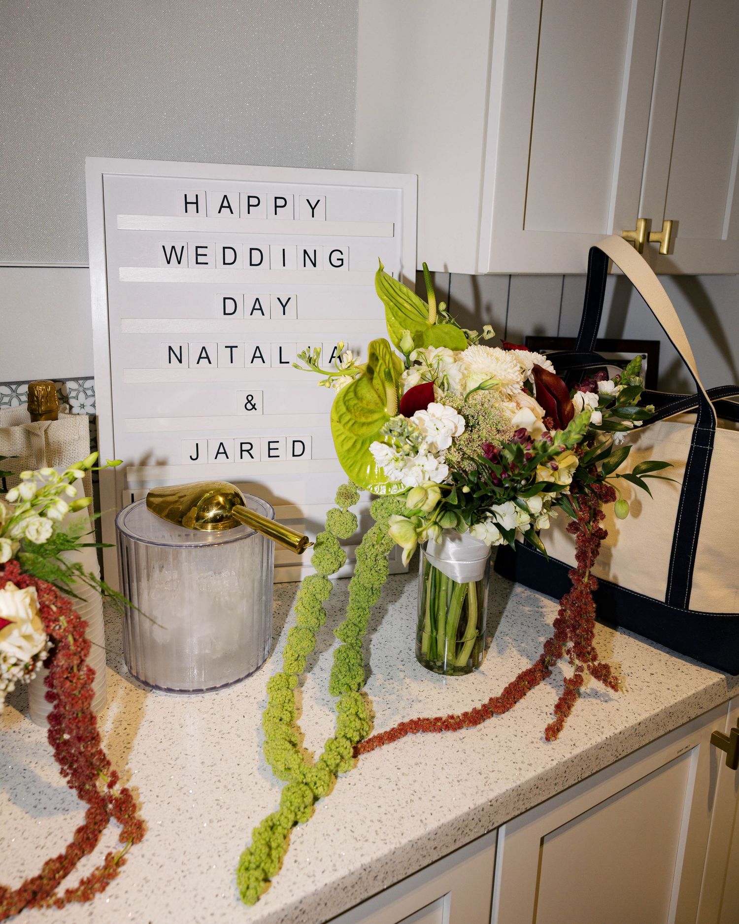 Elegant floral arrangements with green and burgundy stems displayed on a white counter for a wedding.