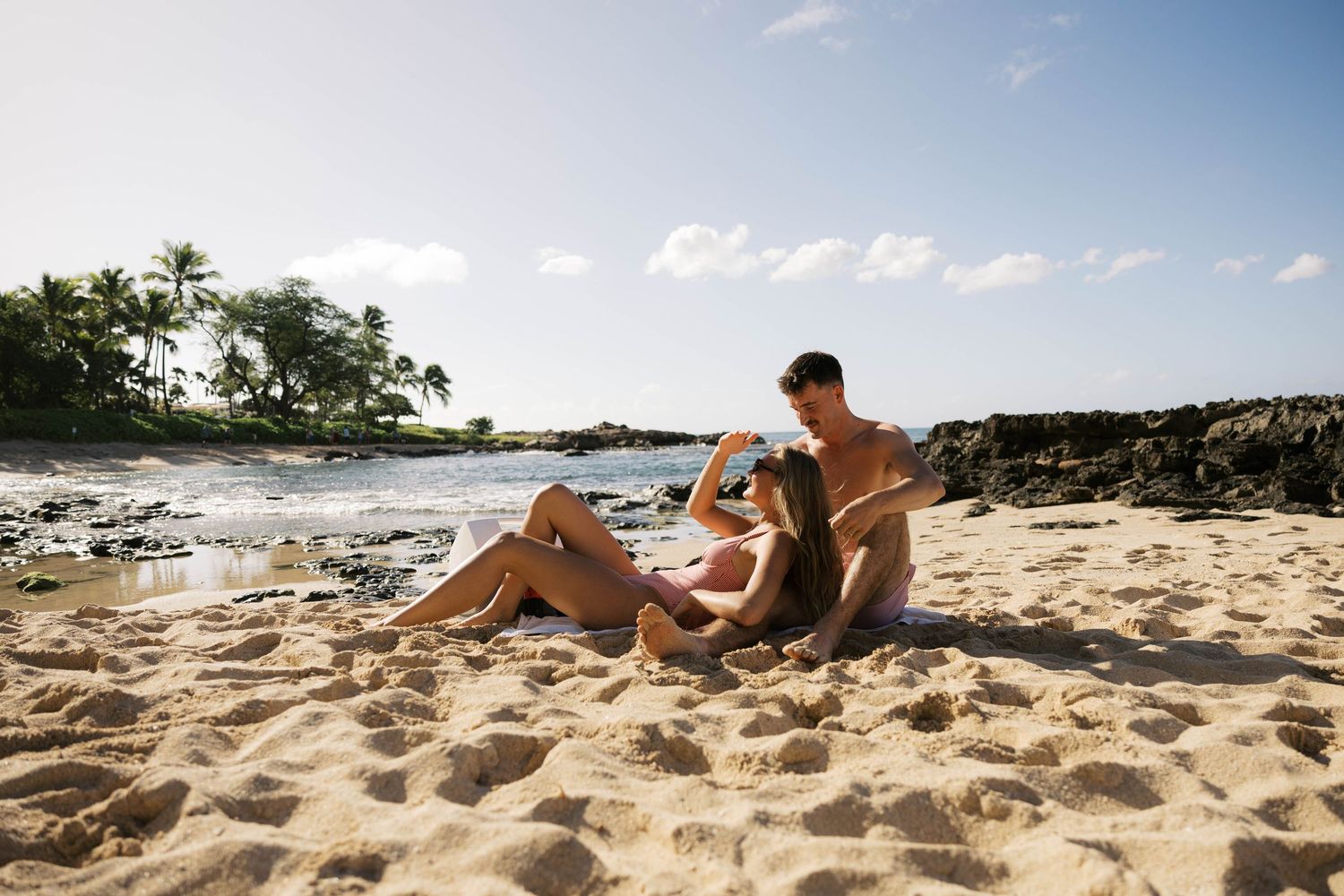 Panoramic view of sandy beach with people relaxing by the ocean on a sunny day.