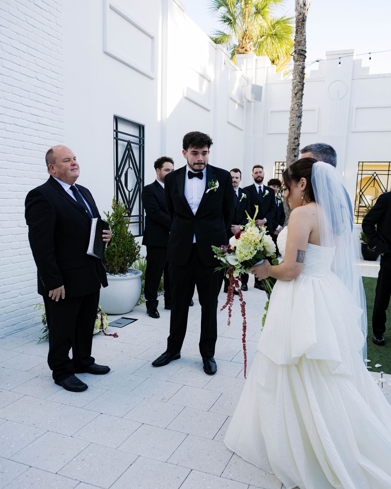 A wedding ceremony taking place in a modern white courtyard with palm trees.