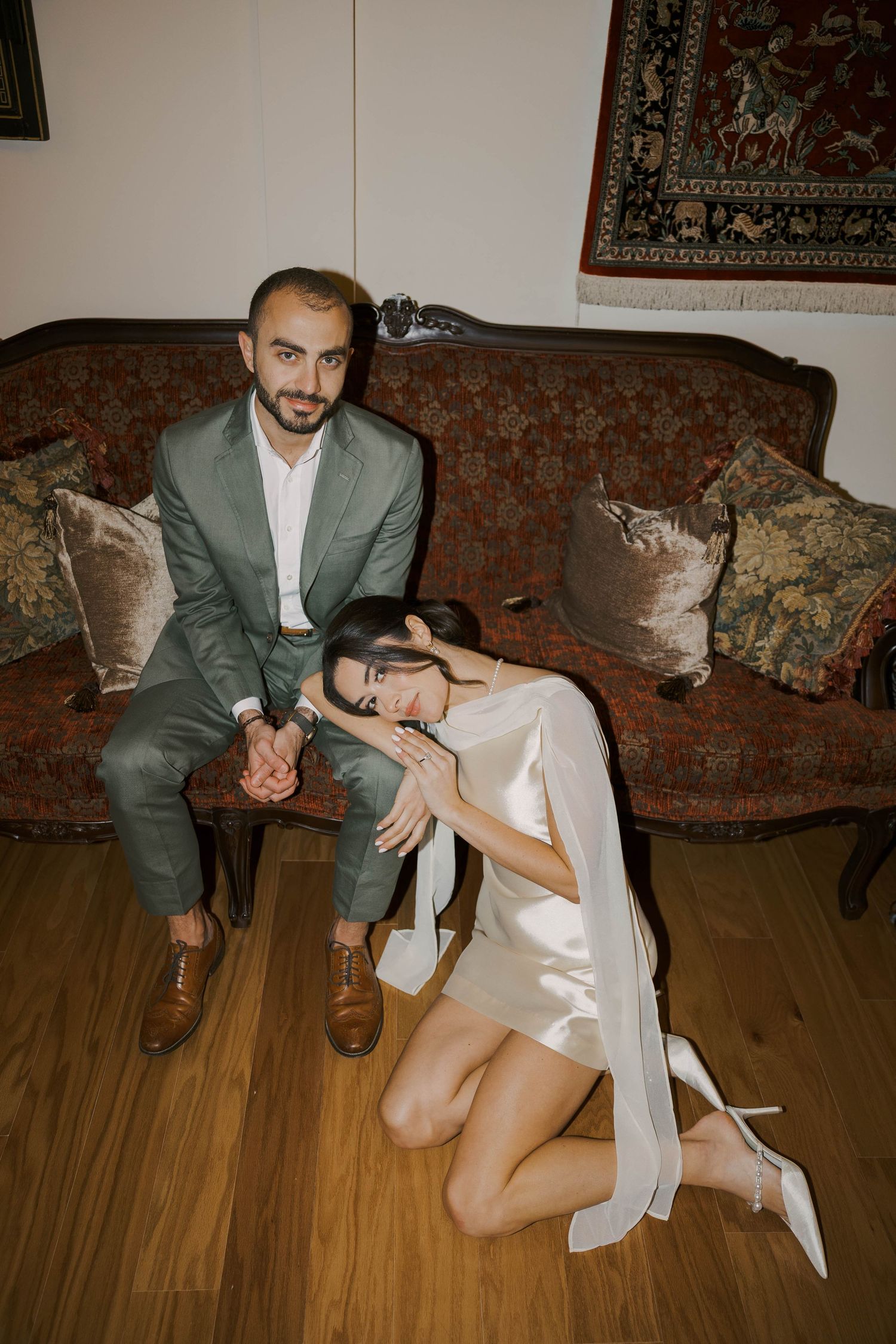 Artistic wedding photography session on vintage couch with ornate rugs in background.
