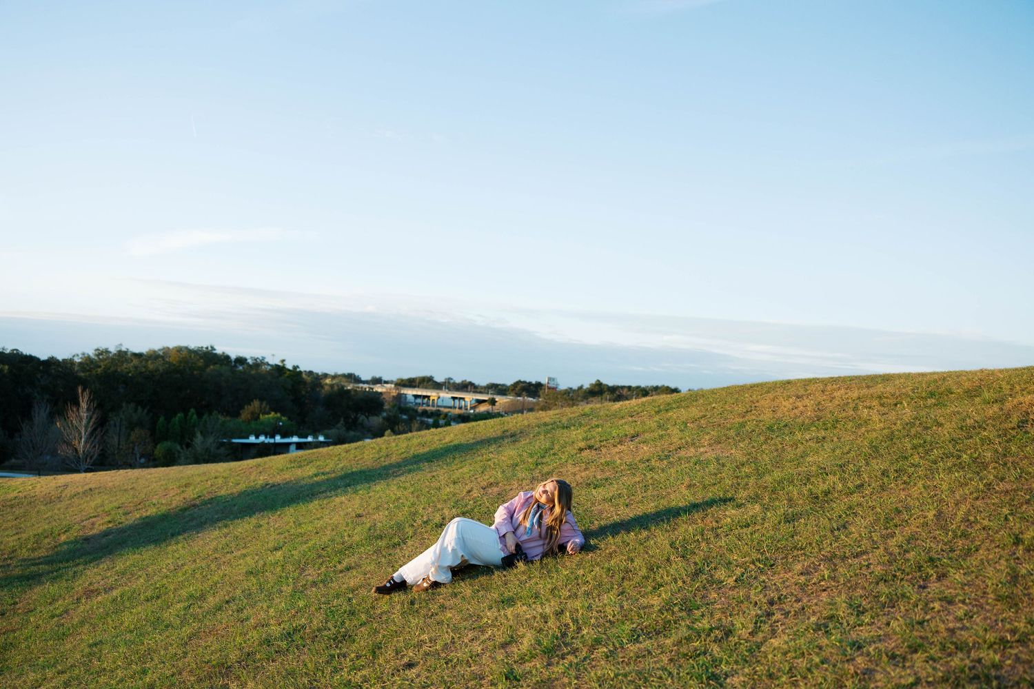 A couple relaxes together on a grassy hillside overlooking a scenic countryside landscape on a sunny day.
