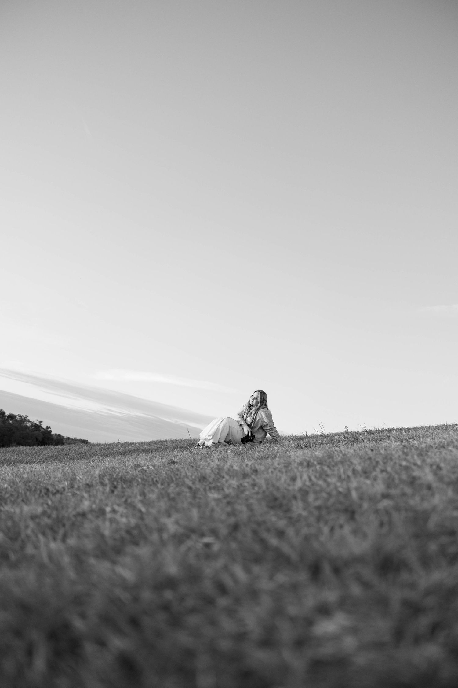 A black and white panoramic view shows a distant figure lying in a grassy field against the horizon.