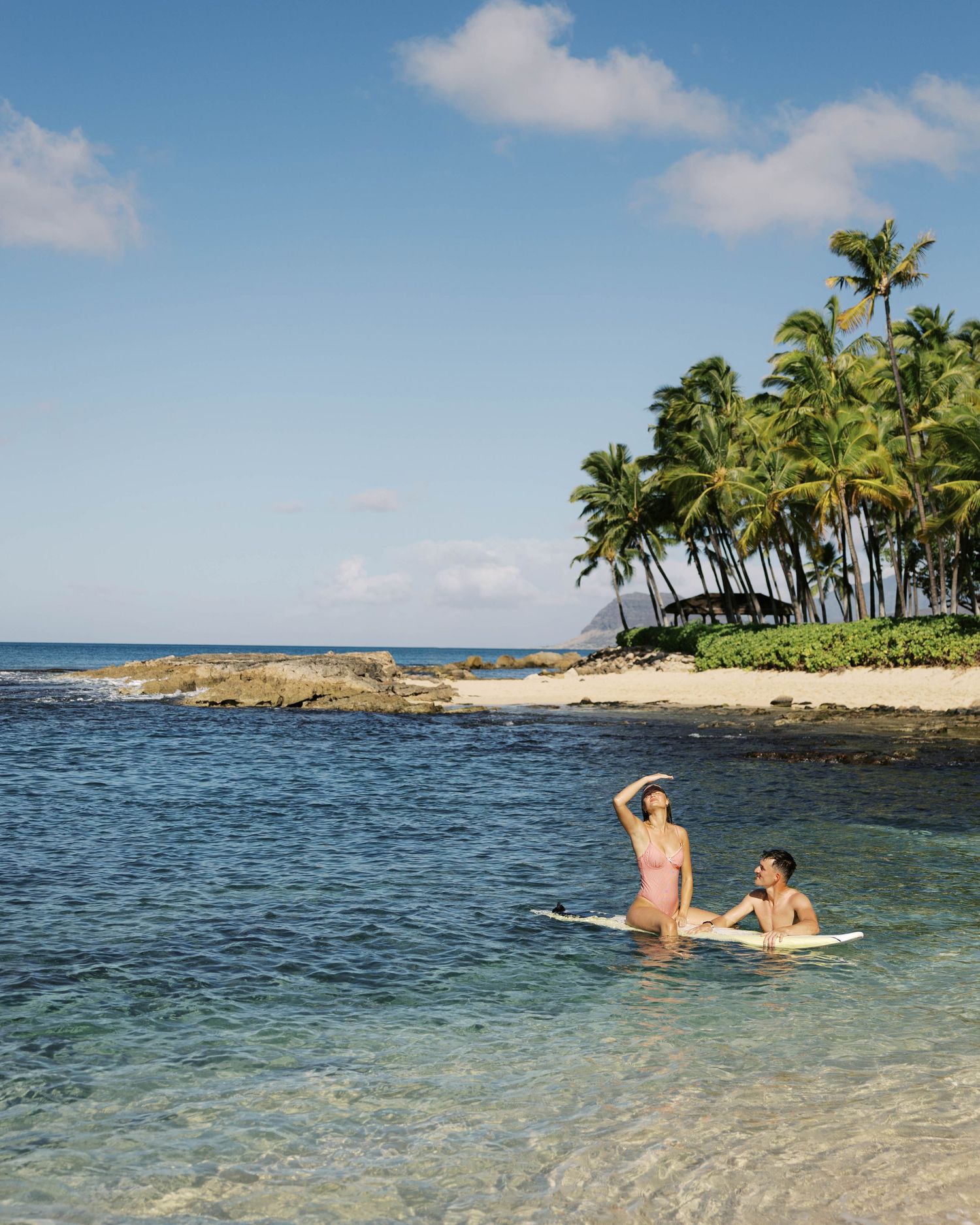 Tropical beach scene with palm trees and swimmers in crystal clear waters.