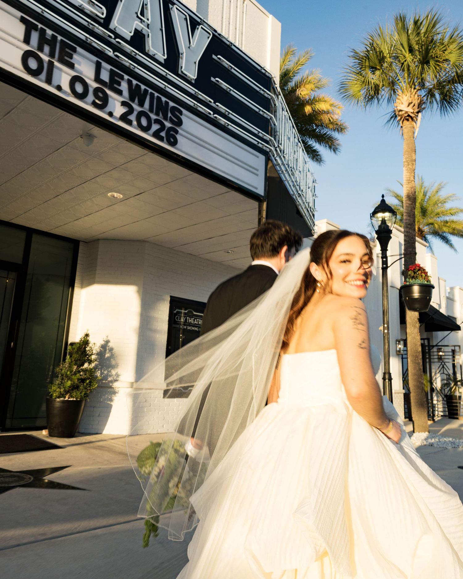 A bride in a voluminous white dress poses against an Art Deco theater facade.
