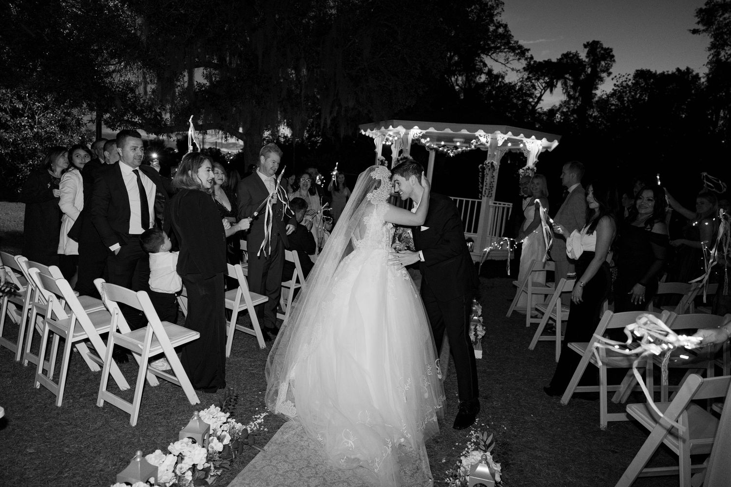 Nighttime wedding ceremony setup with white chairs and floral decorations.