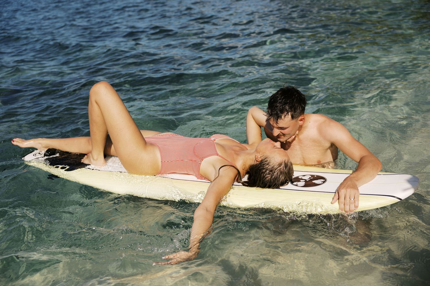 People relaxing on surfboards in clear tropical waters near a palm-lined shore.