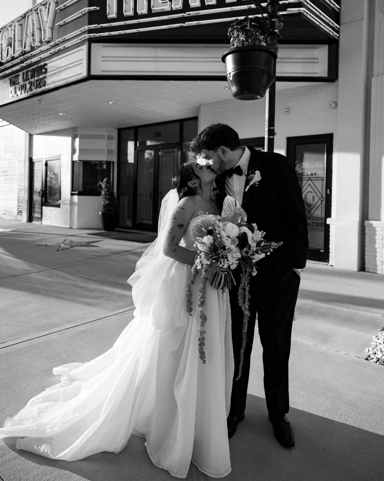 A black and white photo of newlyweds sharing an intimate moment in front of a classic theatre marquee.