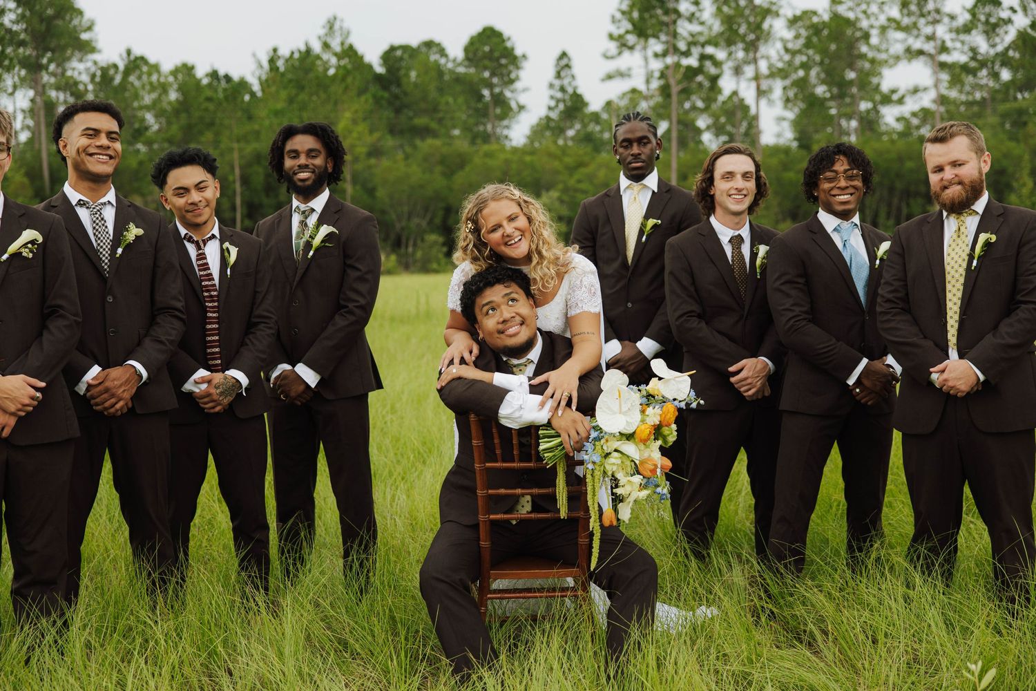 Wedding party in formal attire poses outdoors on green grass.