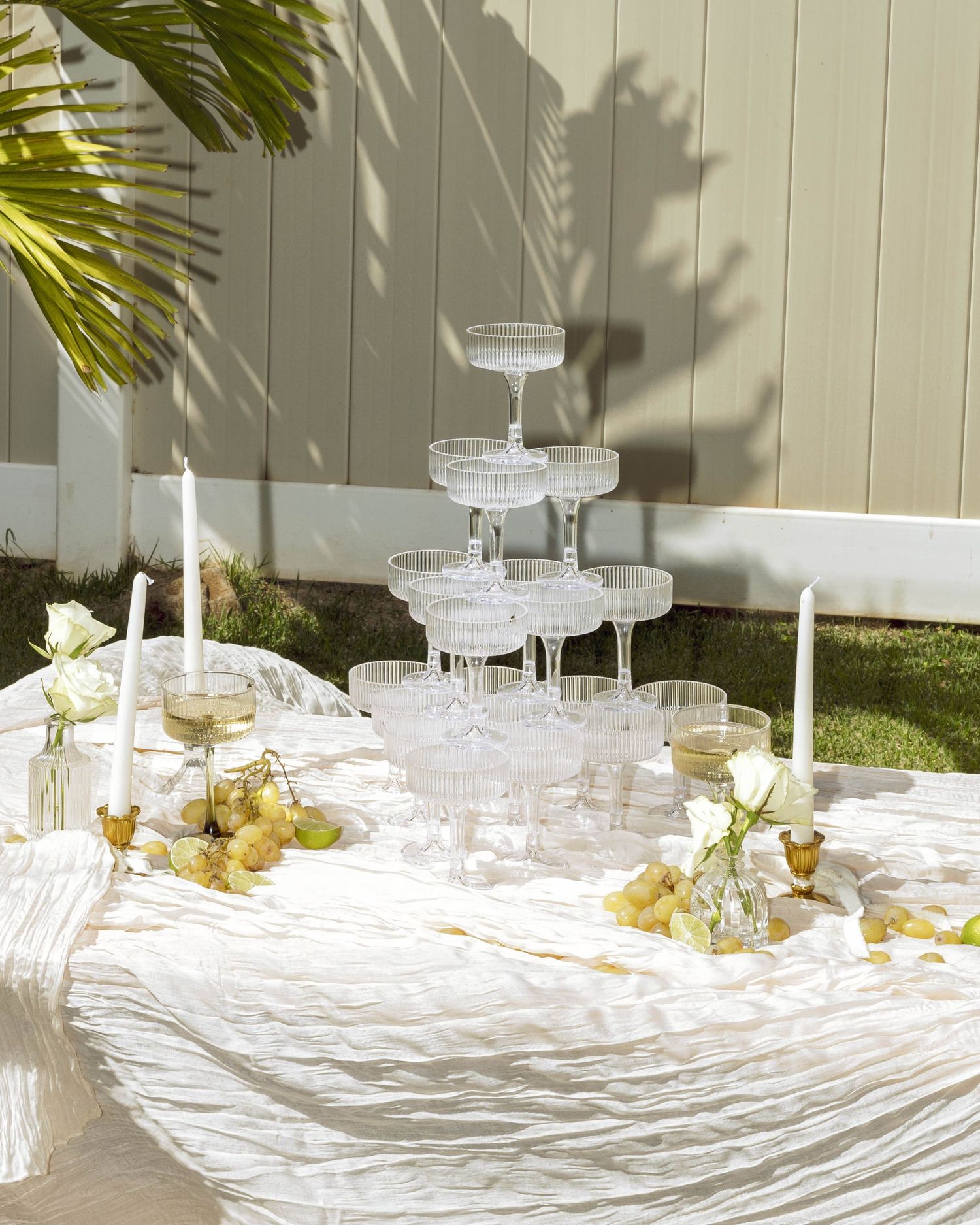 White table settings with glassware and candles create an elegant outdoor dining atmosphere under palm fronds.