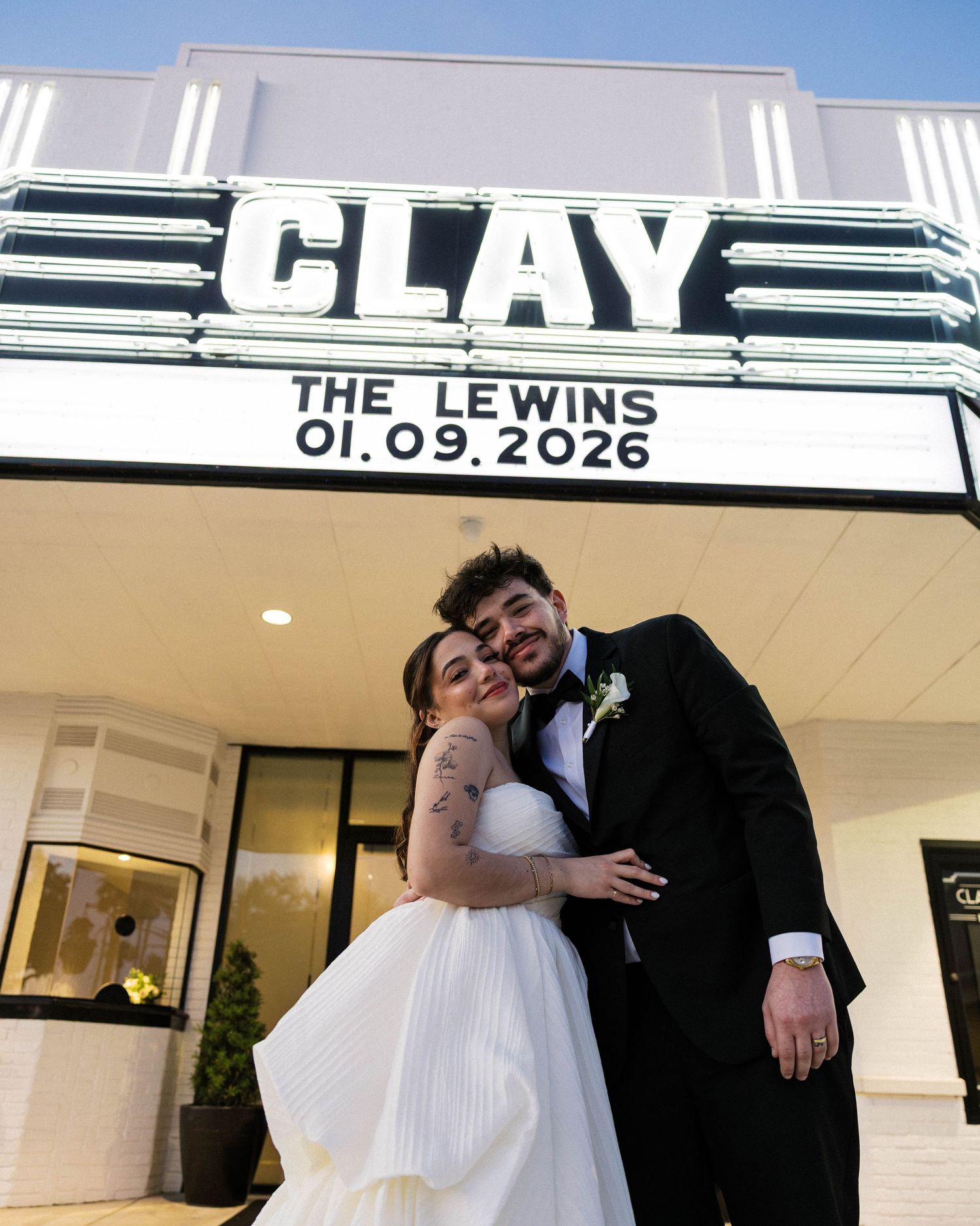 Wedding couple poses beneath illuminated theater sign showing their wedding date.