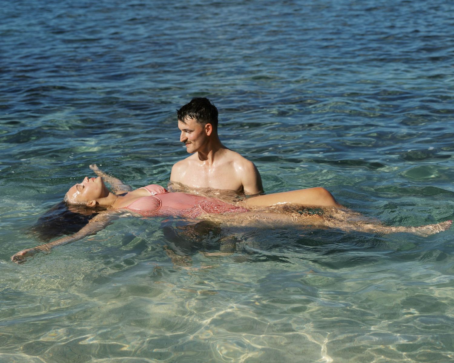 Couple swimming and floating together in clear tropical ocean waters.