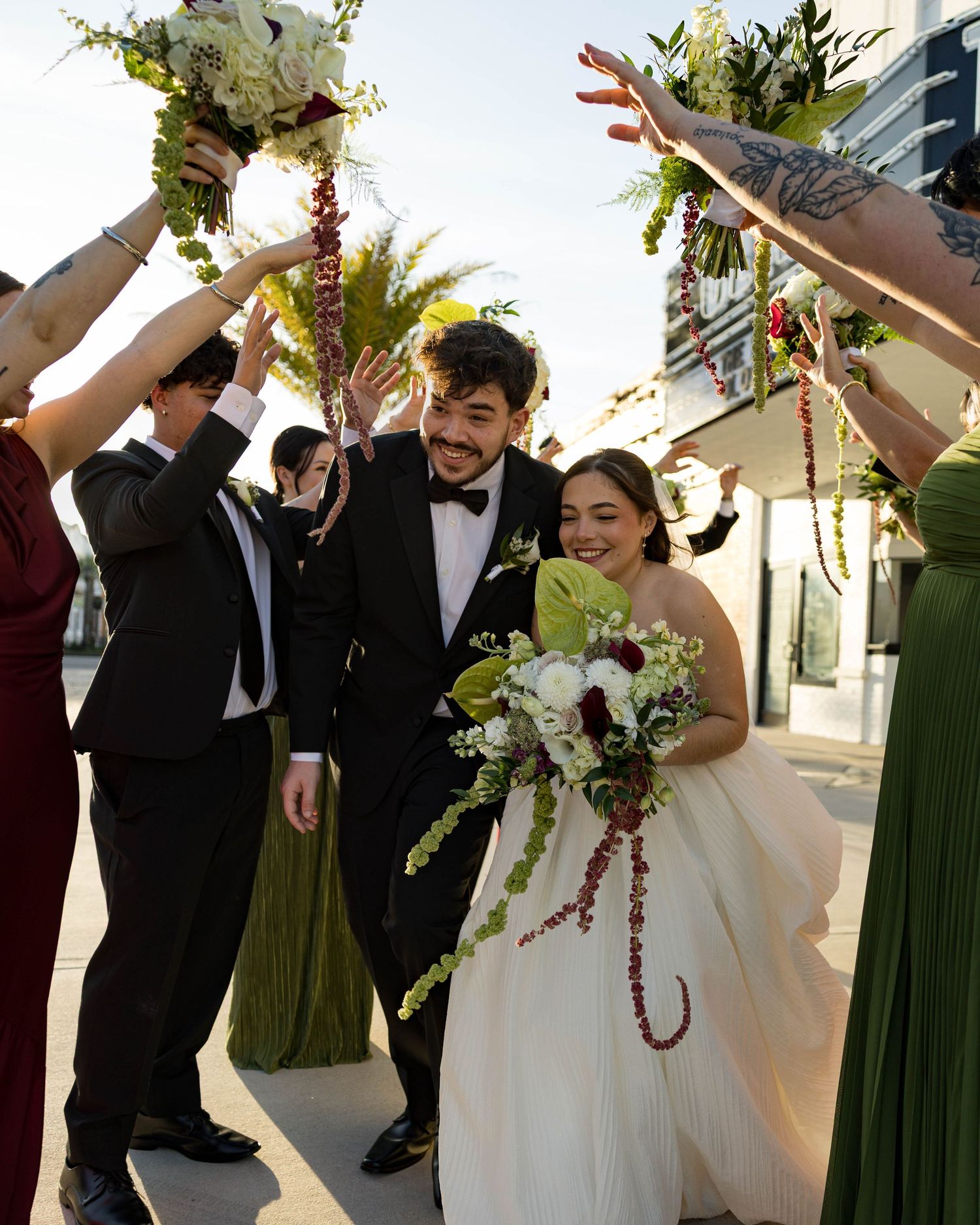 Wedding party celebrates with raised arms and joyful expressions outside theater entrance.