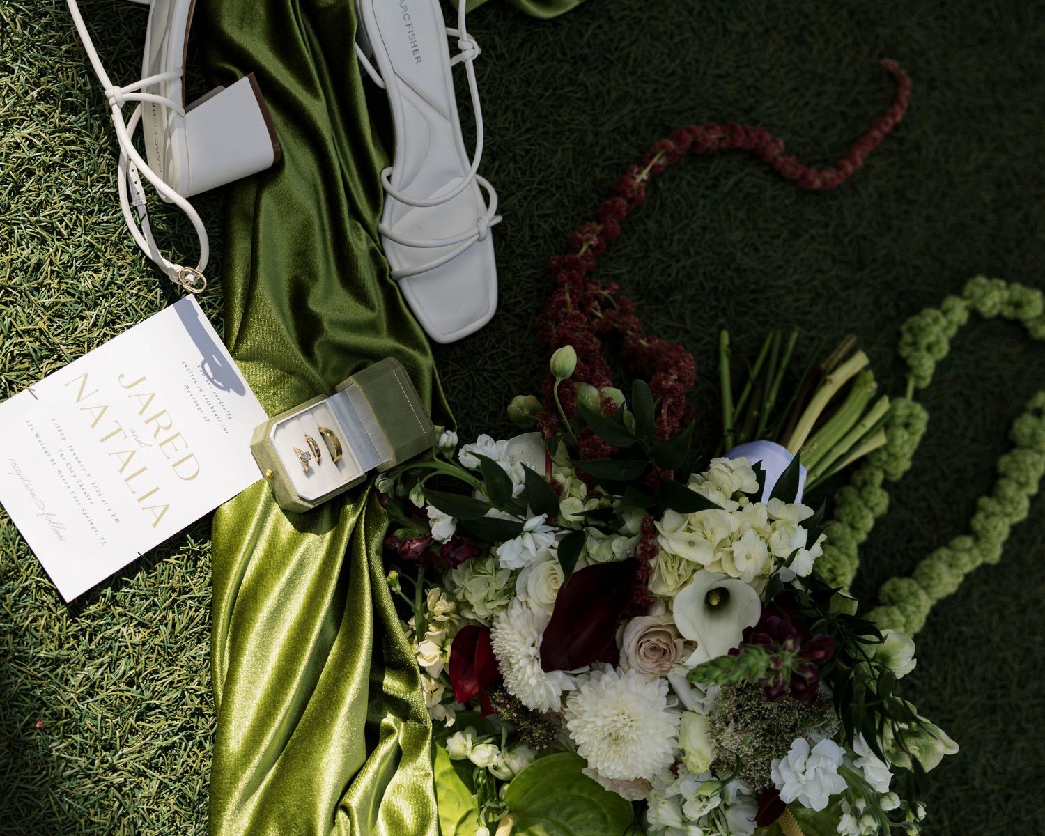 Elegant floral arrangement with white flowers, deep red accents, and lime green anthurium on a chartreuse silk backdrop.