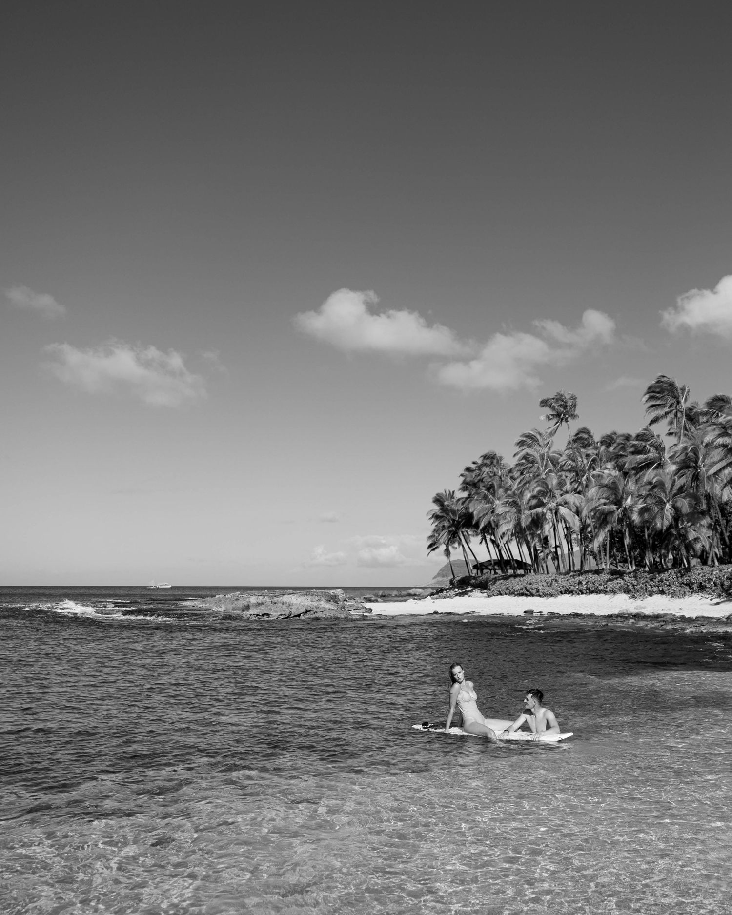 Black and white landscape of tropical beach with palm trees and swimmers in distance.
