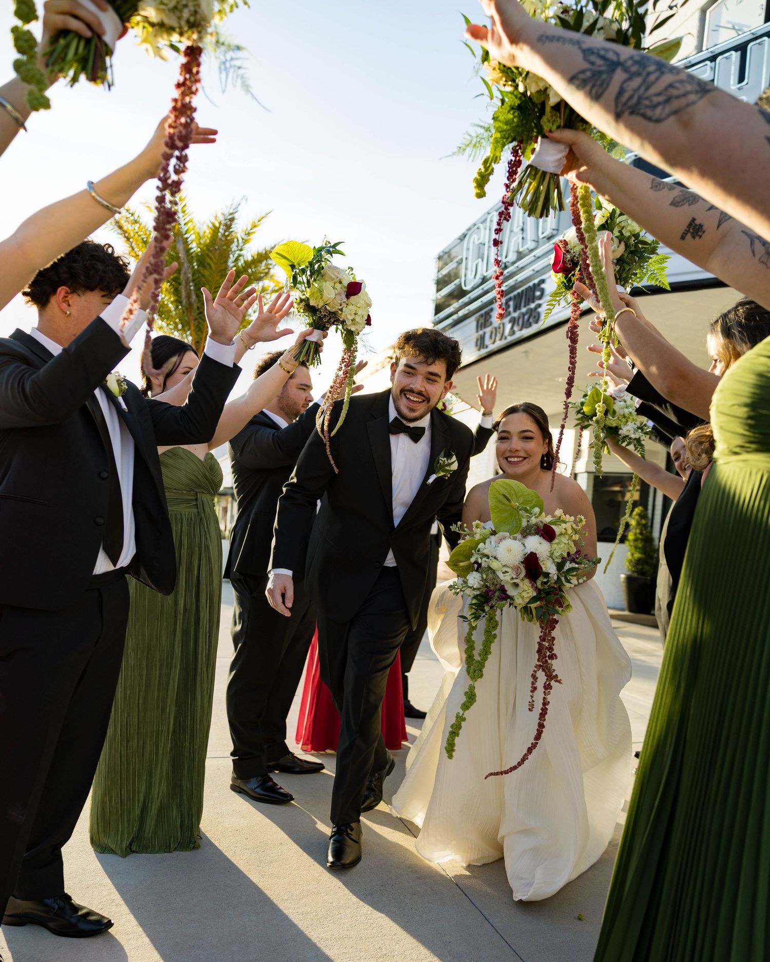 Wedding party celebrating with raised arms outside on a sunny day.
