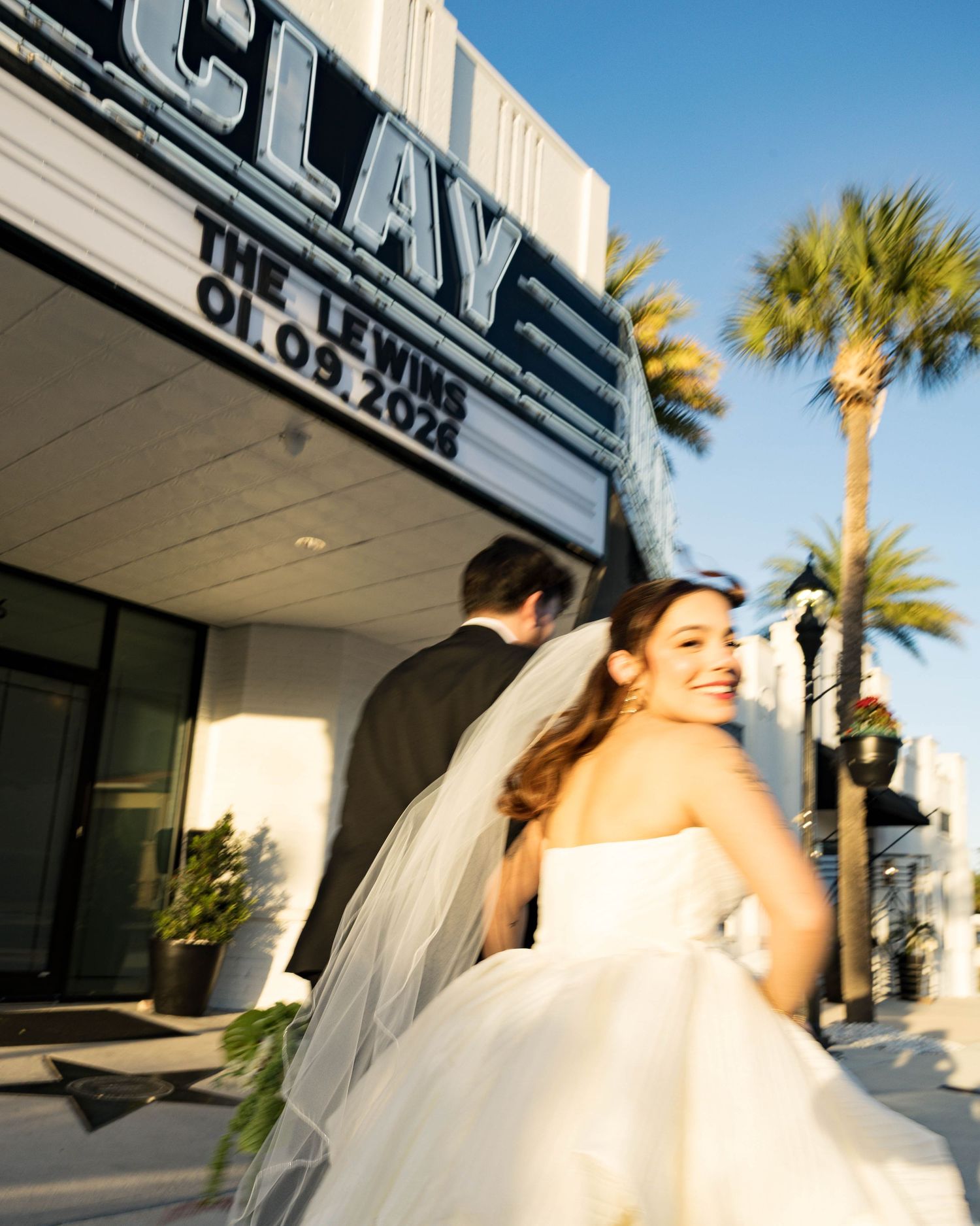A joyful wedding moment captured in motion outside the Clay Theatre with palm trees in view.