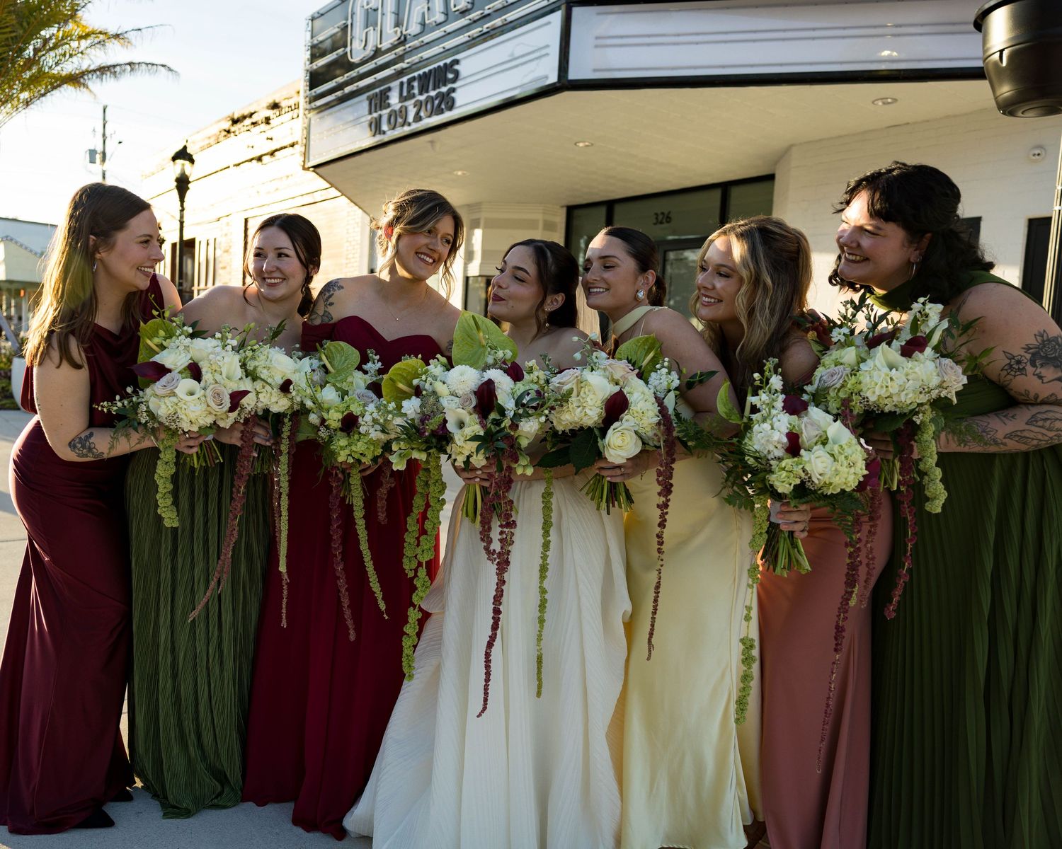 Wedding party members hold bouquets while standing in line against theater wall.