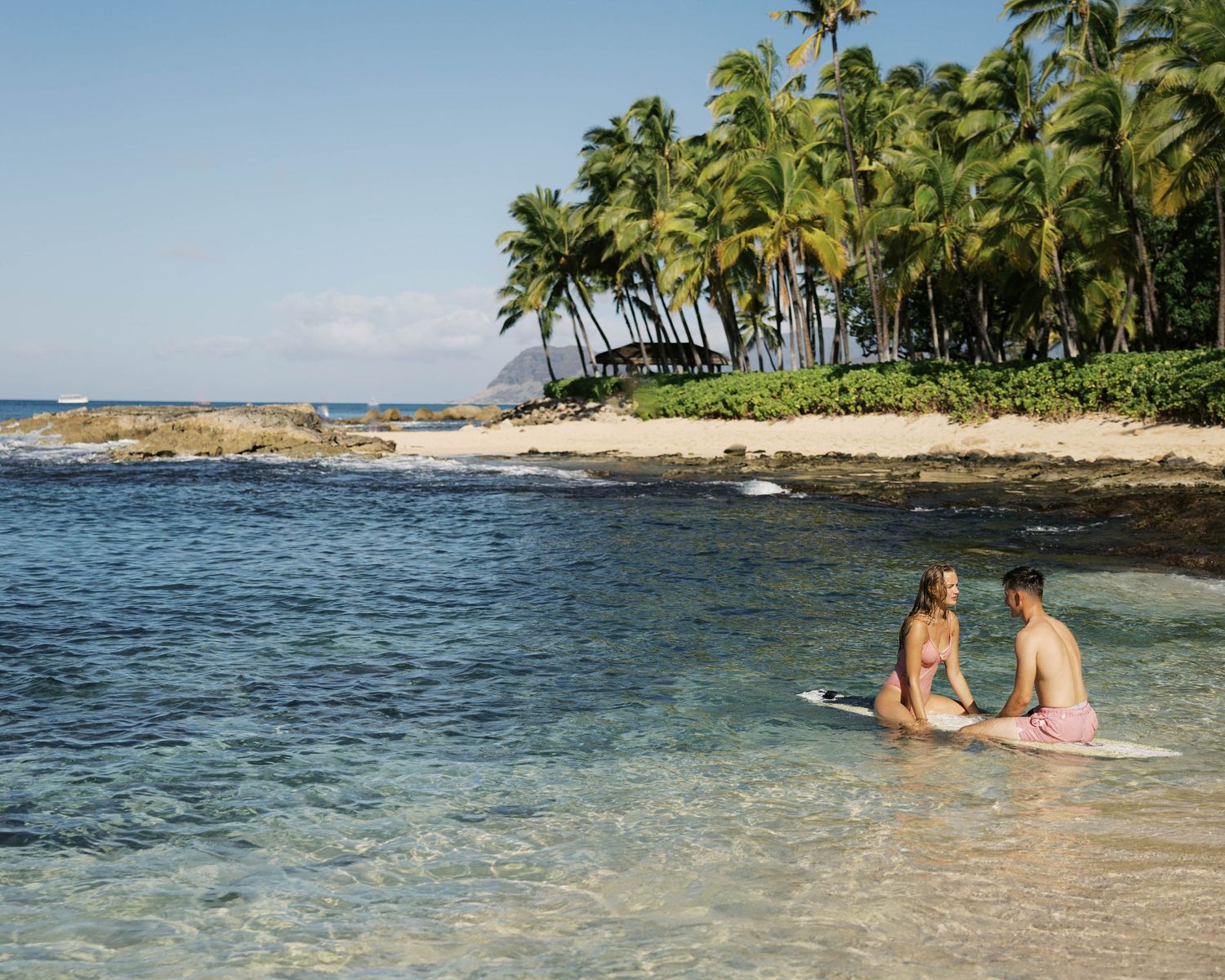Tropical beach scene with palm trees and surfboards floating in calm turquoise waters.