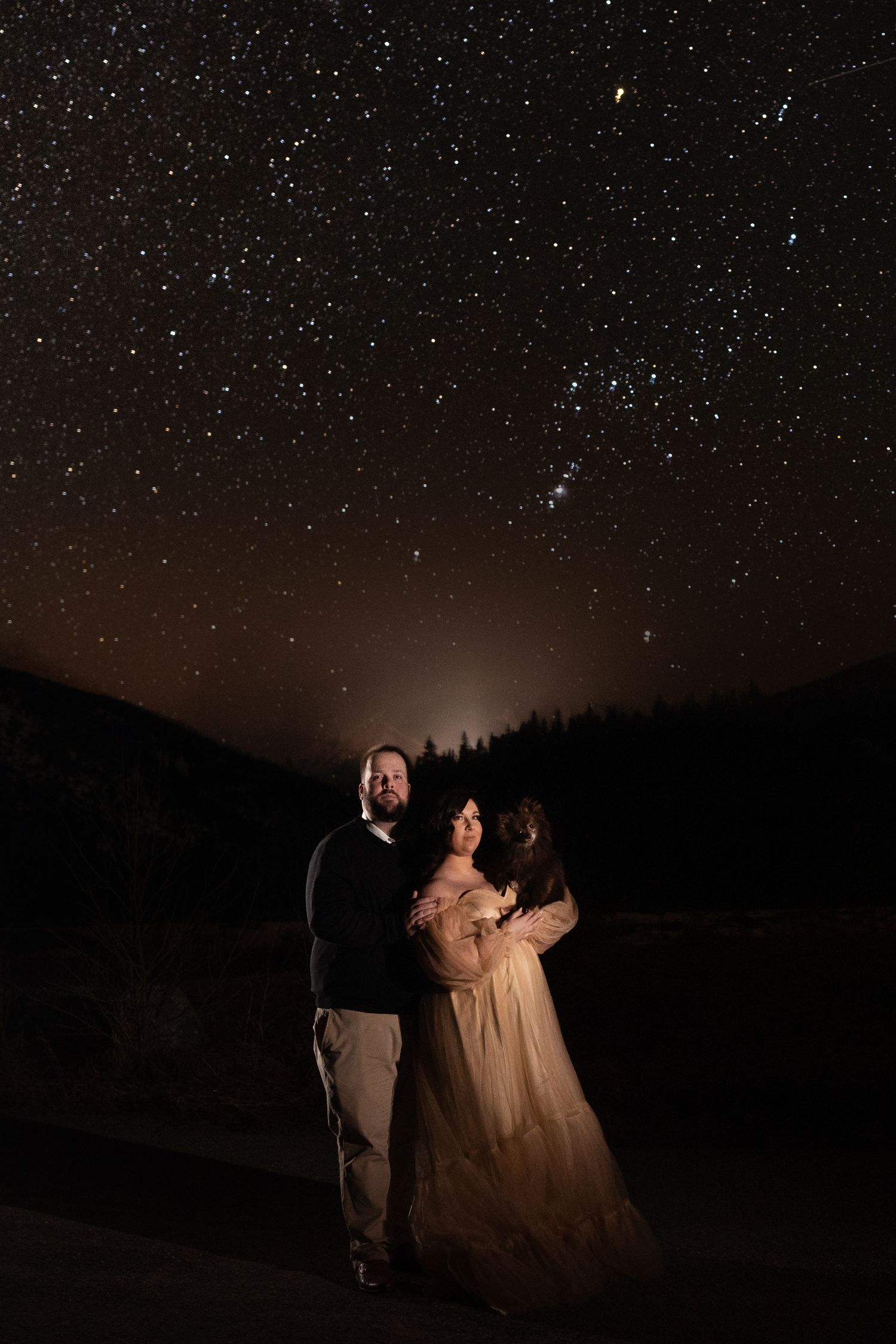 A couple stands together under a starry night sky in a romantic outdoor setting against the Banff landscape in Canada.